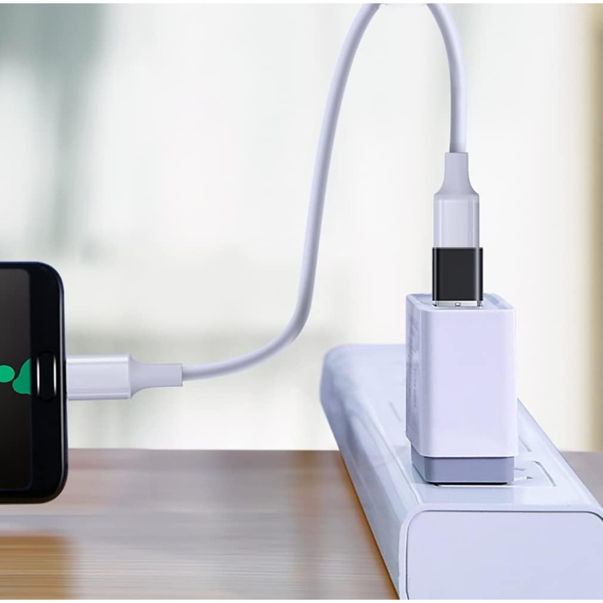 Ein weißes Ladekabel verbindet ein Smartphone mit einem Wandadapter in einer Steckdosenleiste auf einem Tisch.