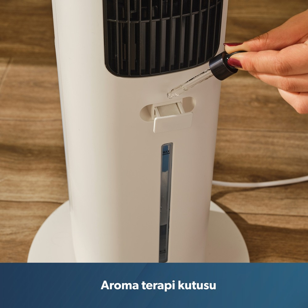 Ahşap zemindeki beyaz kule vantilatörün aroma haznesine damlalıkla uçucu yağ ekleyen bir el.