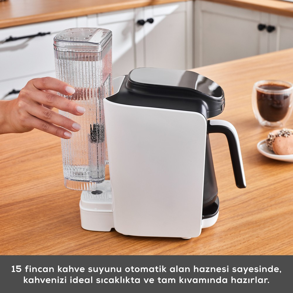 Bir el, ahşap masadaki beyaz ve siyah kahve makinesine su haznesini takıyor.
