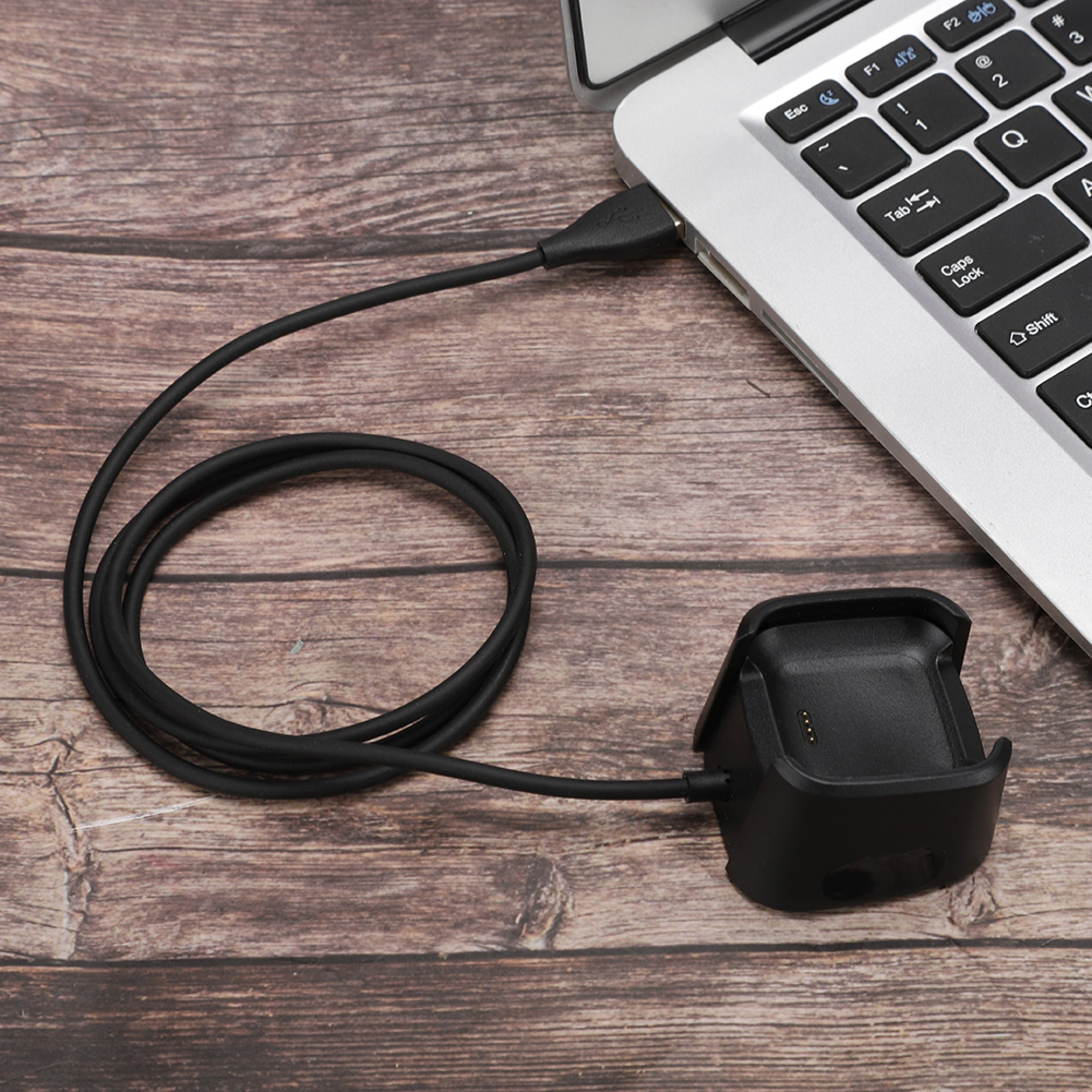 Ein schwarzes Ladekabel ist an einen Laptop angeschlossen und liegt auf einer Holzoberfläche.