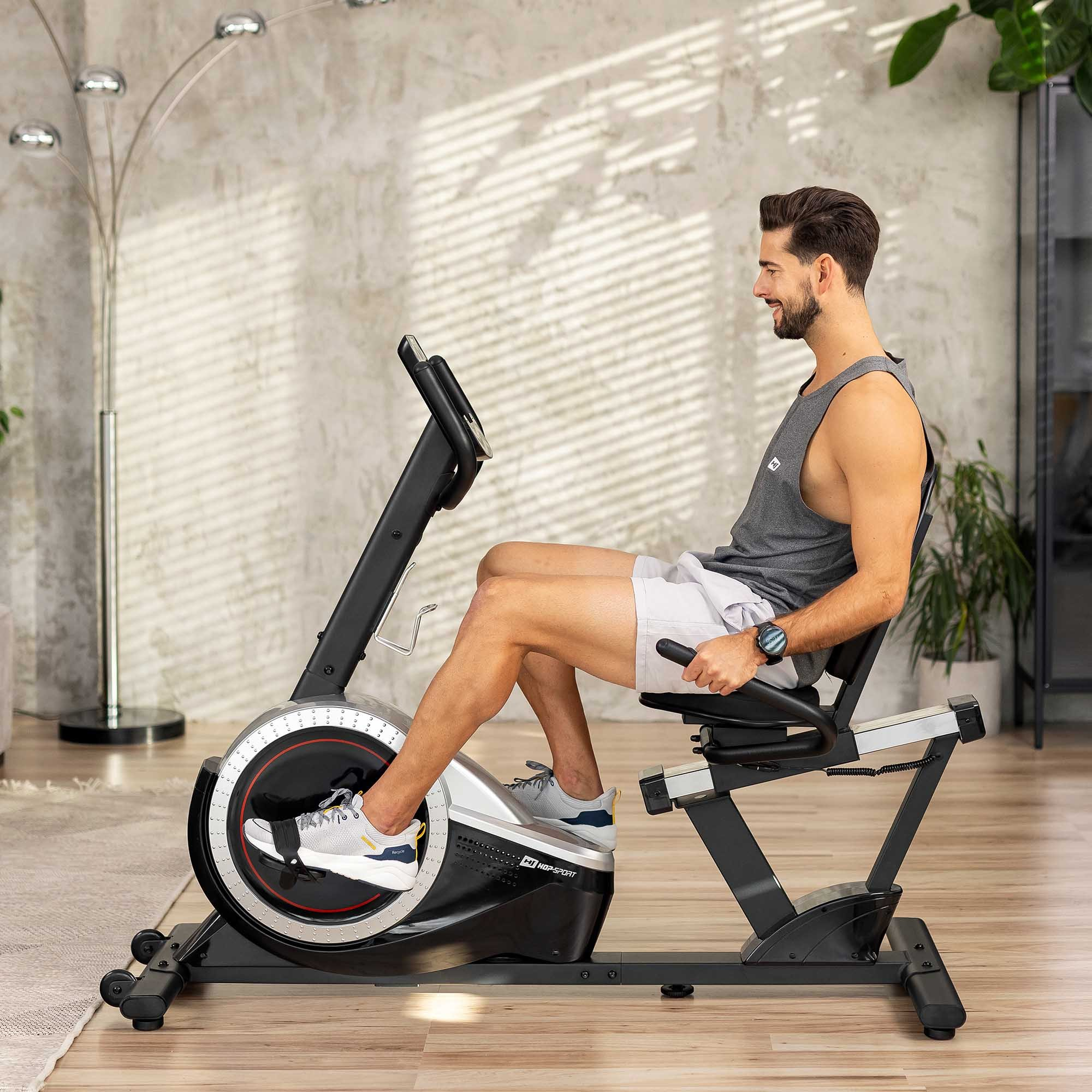 Ein Mann in Sportkleidung sitzt auf einem Heimtrainer in einem hellen Raum.