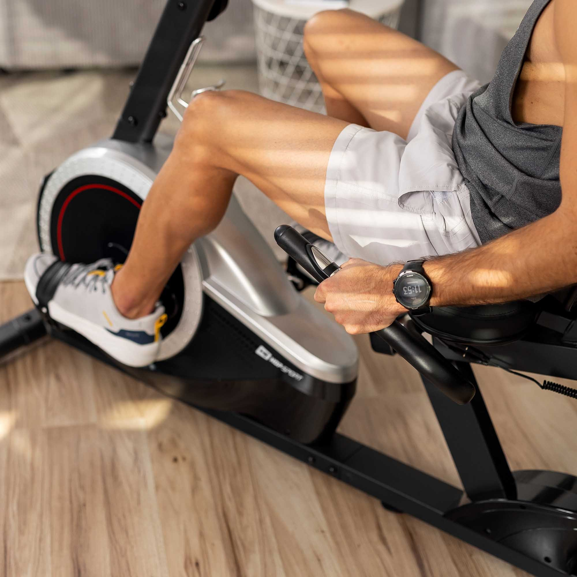 Ein Mann in Sportkleidung trainiert auf einem Heimtrainer in einem hellen Raum.