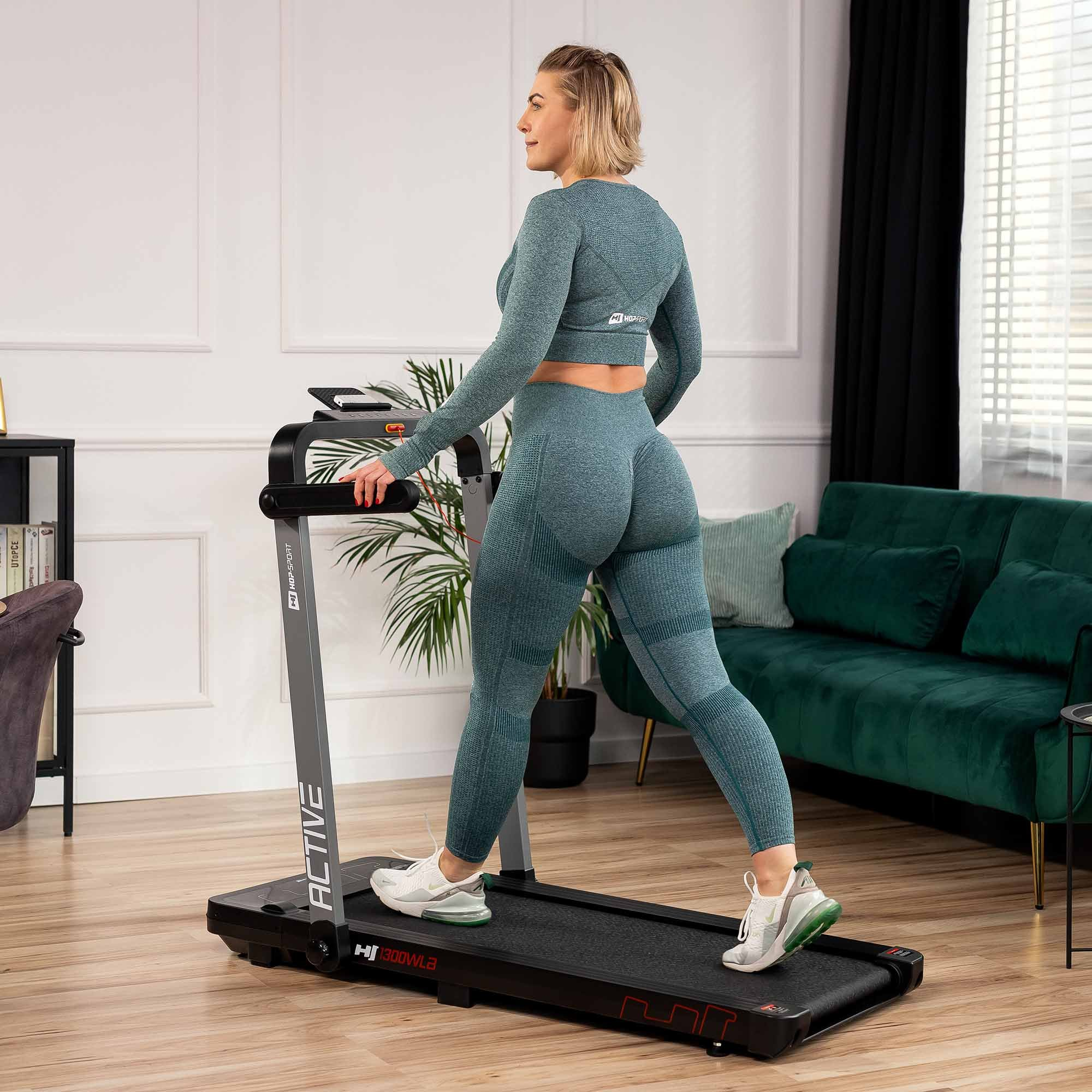 Eine Frau in tealfarbener Sportbekleidung geht auf einem schwarzen Laufband in einem hellen Raum.