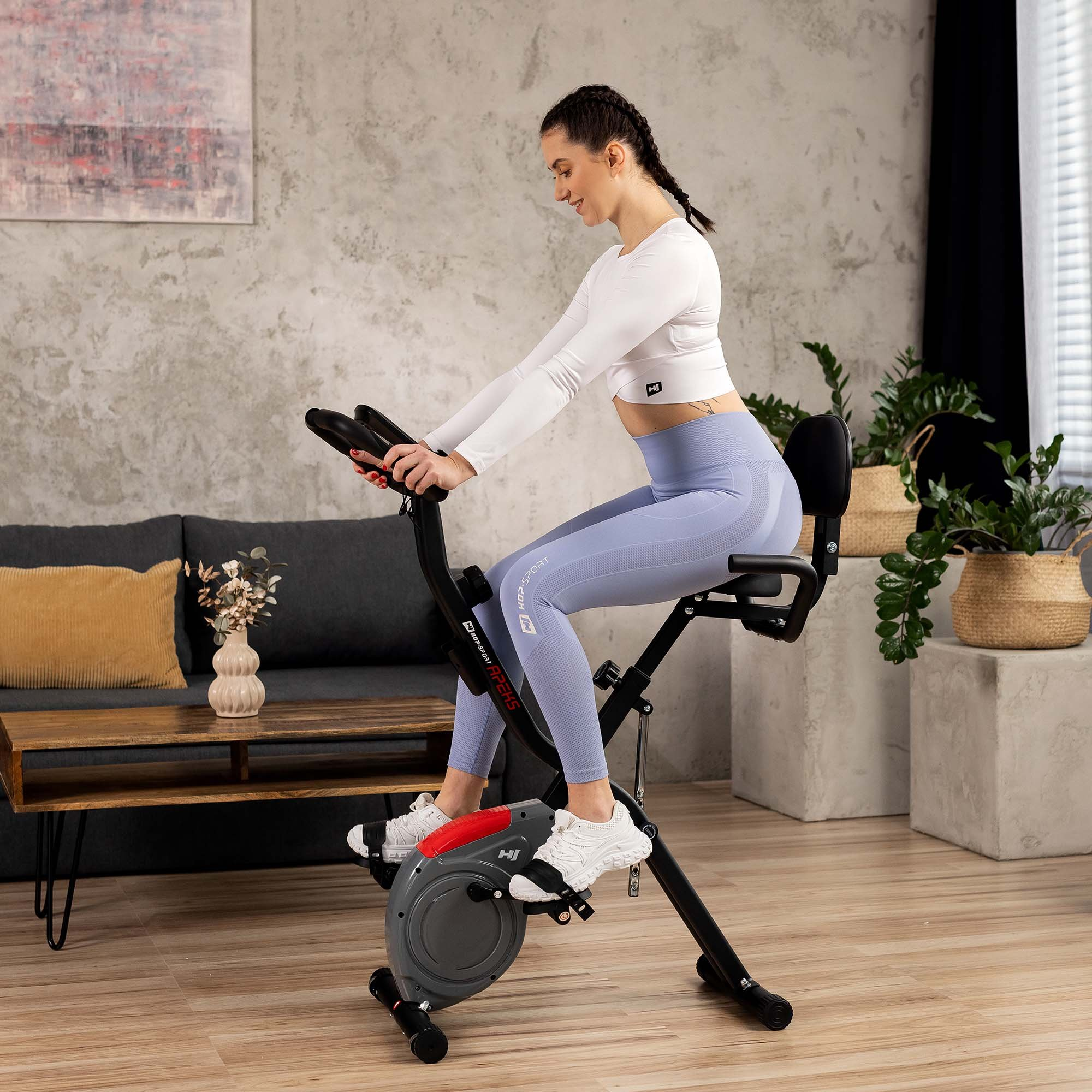 Eine Frau in Sportbekleidung trainiert auf einem Heimtrainer in einem modern eingerichteten Wohnzimmer.