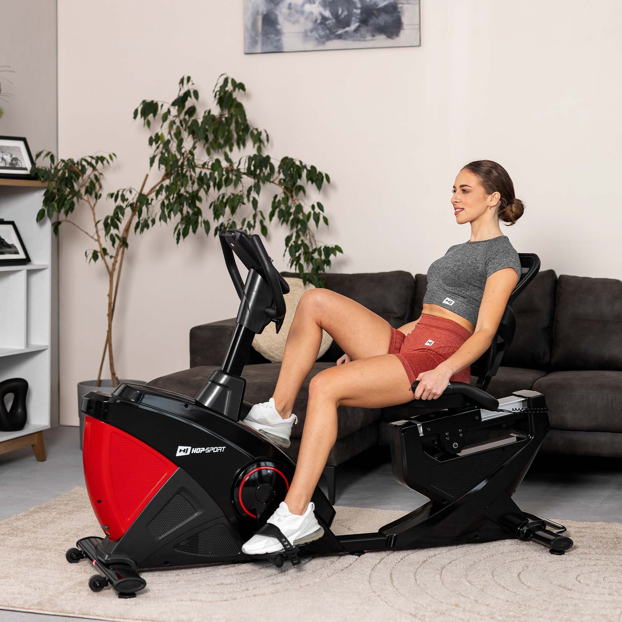 Eine Frau in Sportkleidung trainiert zu Hause auf einem schwarzen und roten Liegehefter.