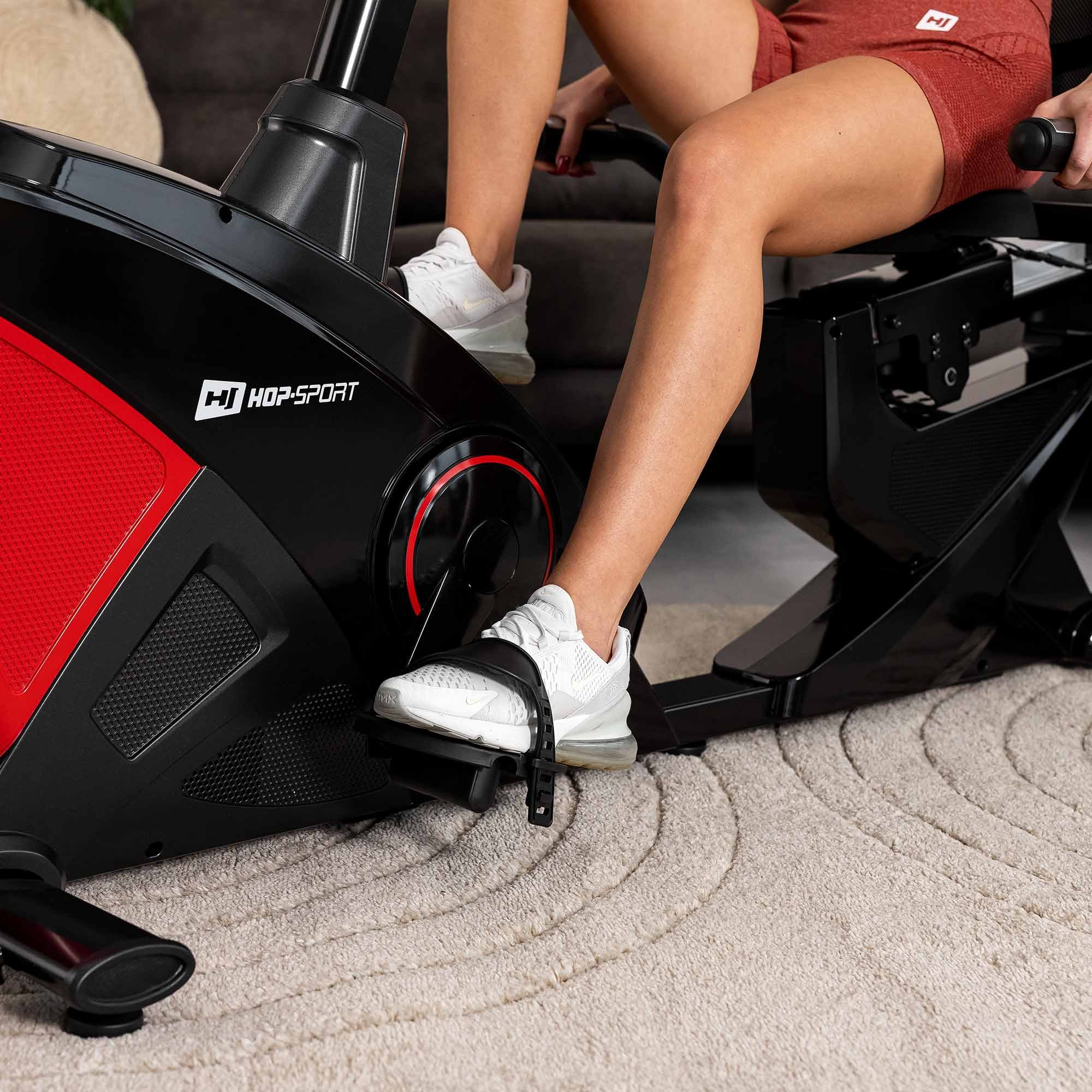 Eine Frau in Sportkleidung nutzt ein schwarzes und rotes Hop-Sport Heimfahrrad auf einem Teppich.