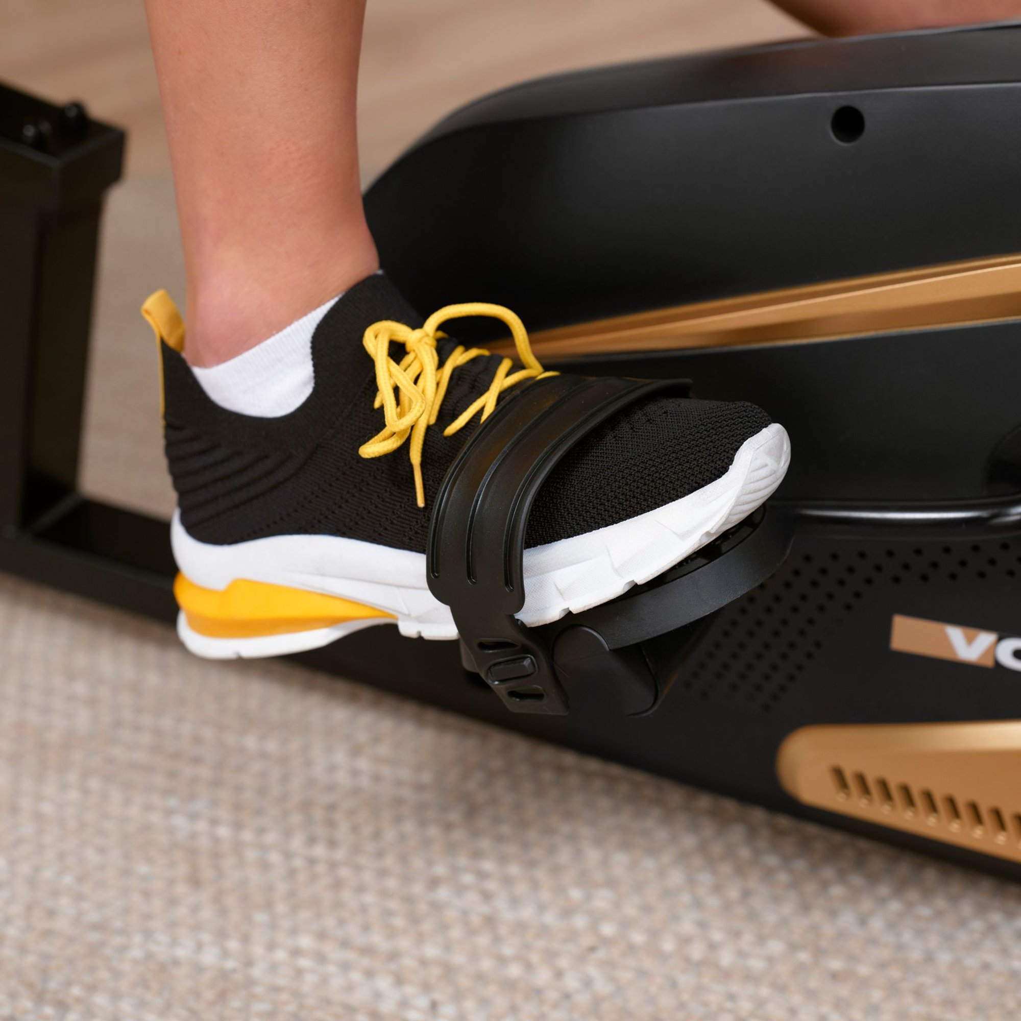 Ein Fuß in einem schwarzen und gelben Sneaker sichert sich im Pedal eines Crosstrainers.