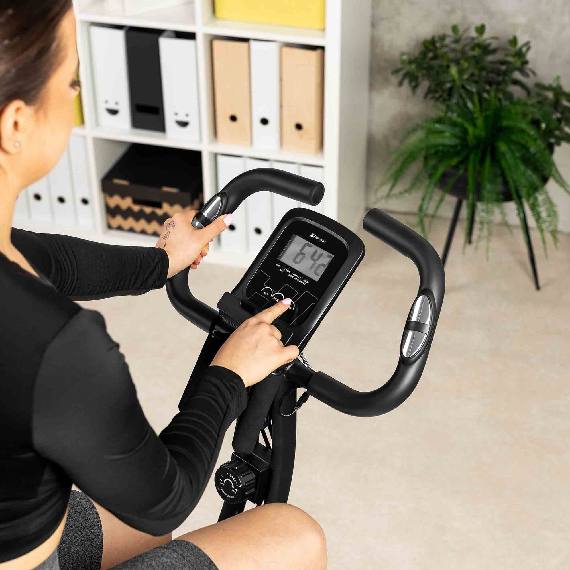 Eine Frau in Sportkleidung sitzt auf einem Heimtrainer und bedient das Display.