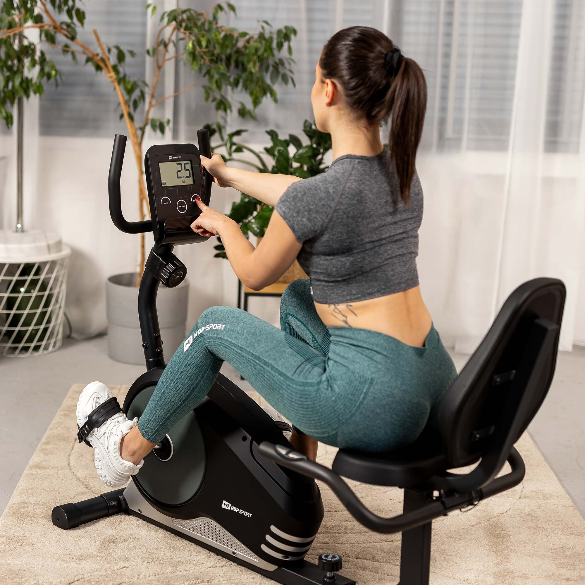 Eine Frau in Sportkleidung sitzt auf einem Heimtrainer und bedient das Display.