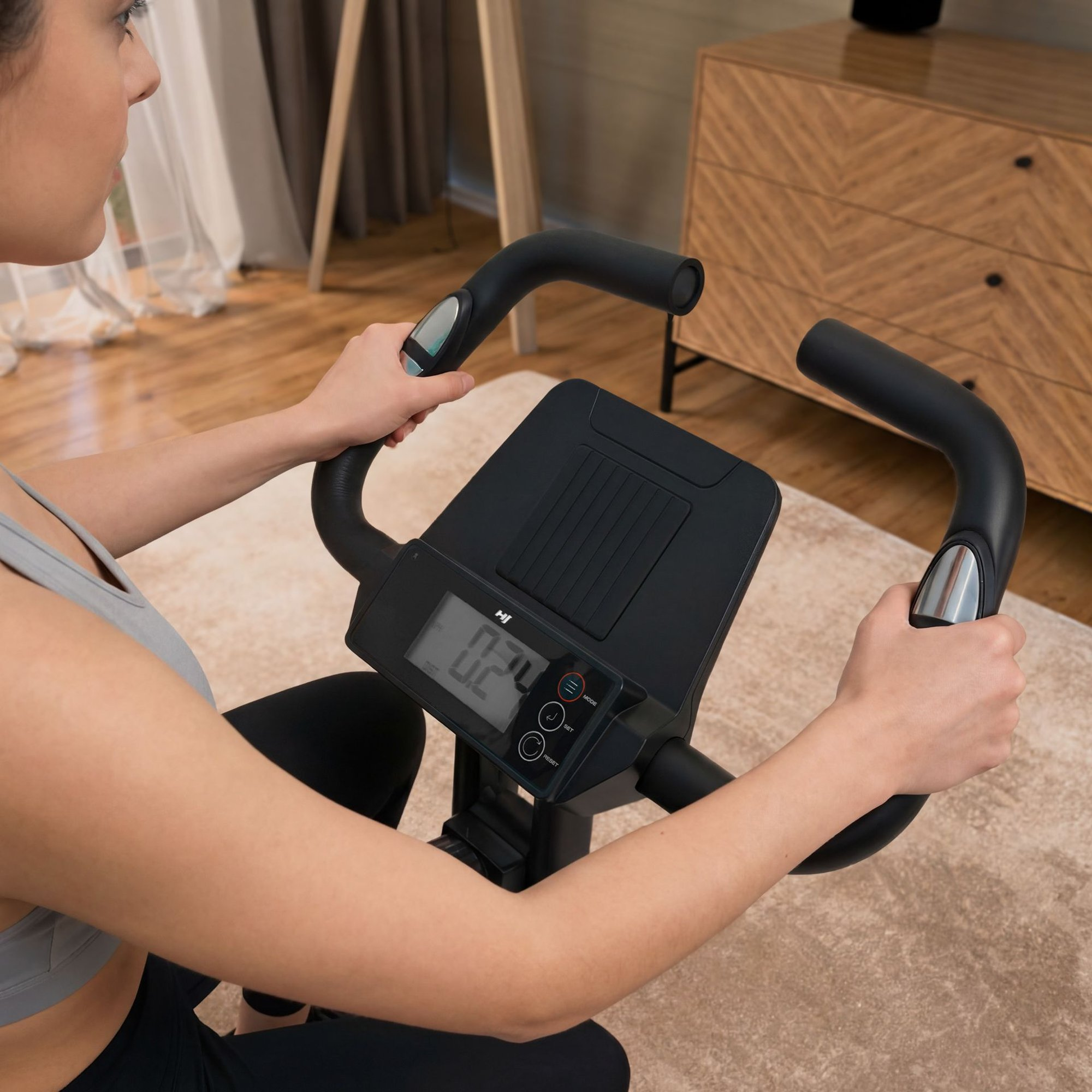 Eine Frau in Sportbekleidung trainiert auf einem Heimtrainer in einem hellen Wohnzimmer.