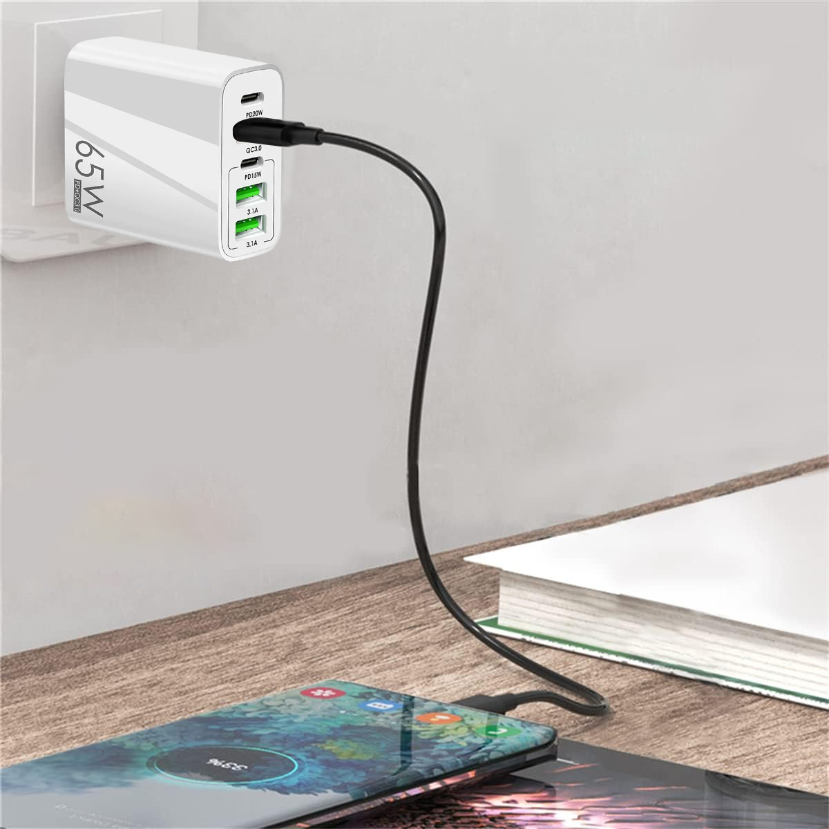 Ein weißes 65W USB-Ladegerät steckt in der Wand, ein schwarzes Kabel lädt ein Smartphone auf einem Holztisch.