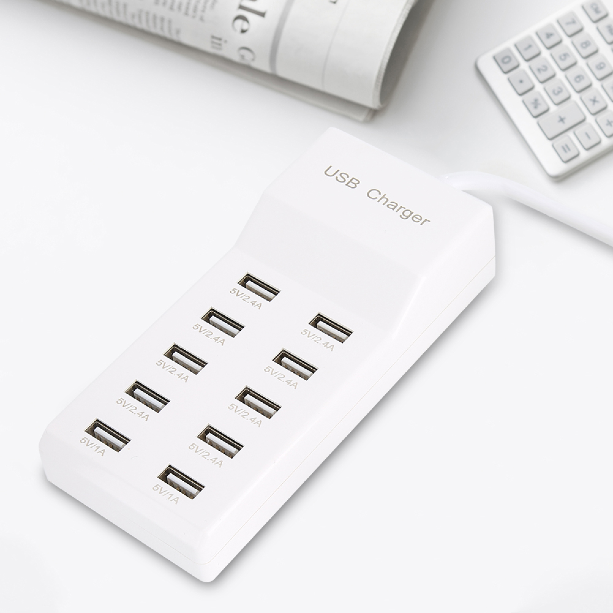 Ein weißer USB-Ladehub mit zehn Anschlüssen auf weißem Tisch mit Taschenrechner.
