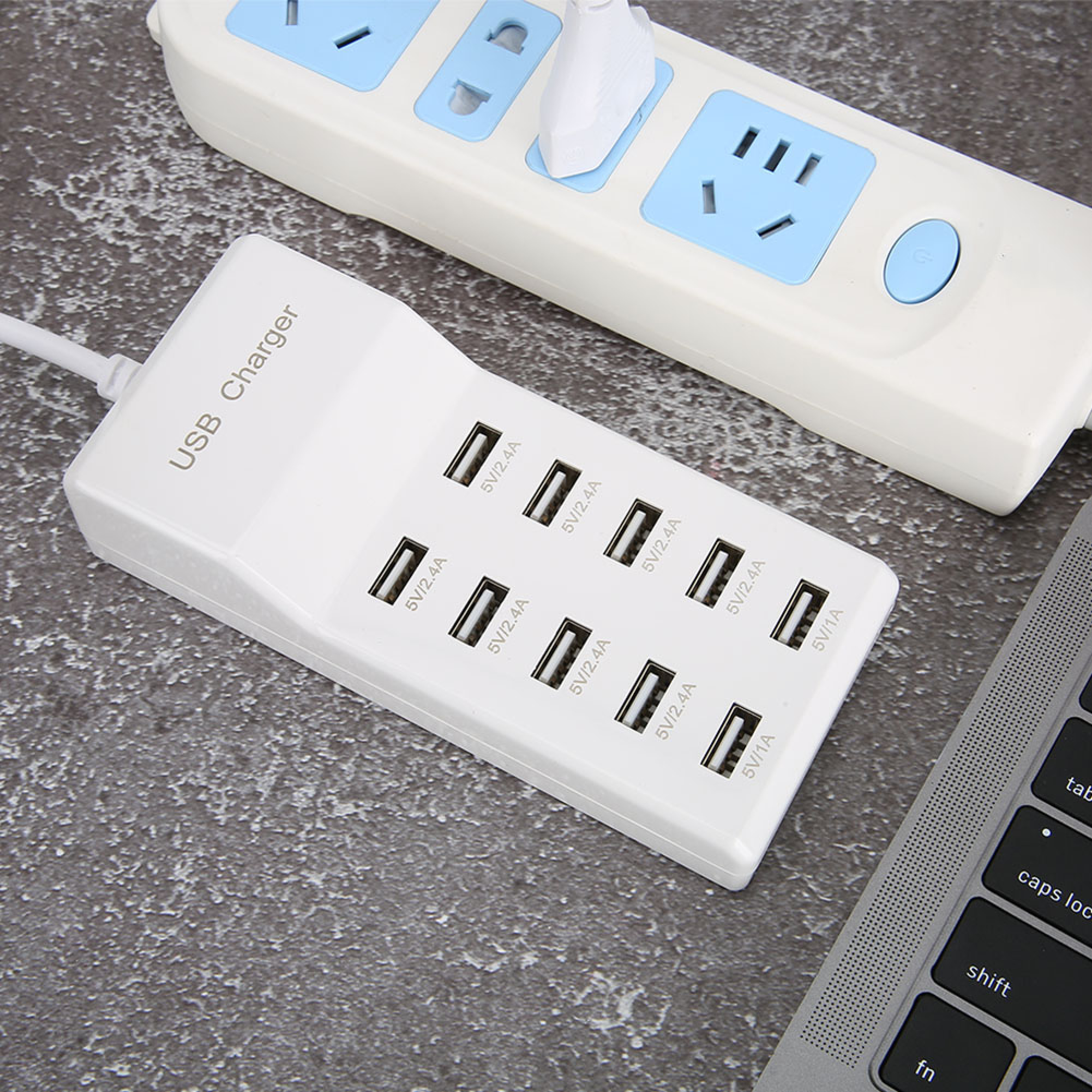 Ein weißer USB-Lader mit zehn Anschlüssen, verbunden mit einer Steckdosenleiste auf einer grauen Oberfläche.