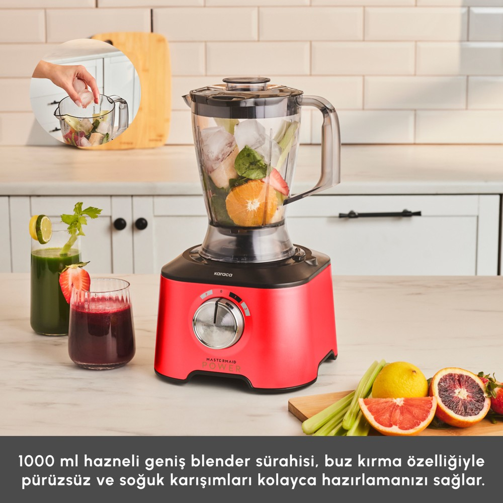 Meyve ve buz dolu kırmızı bir blender, meyve suları ve taze malzemelerin yanında beyaz tezgahta duruyor.