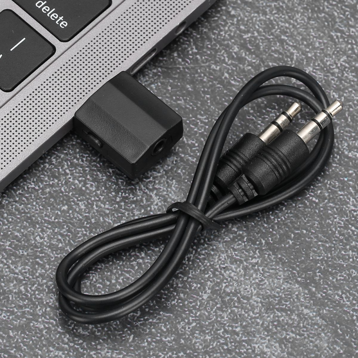 Ein schwarzes Audiokabel mit zwei Klinkensteckern und einem Adapter neben einem Laptop auf einer grauen Oberfläche.