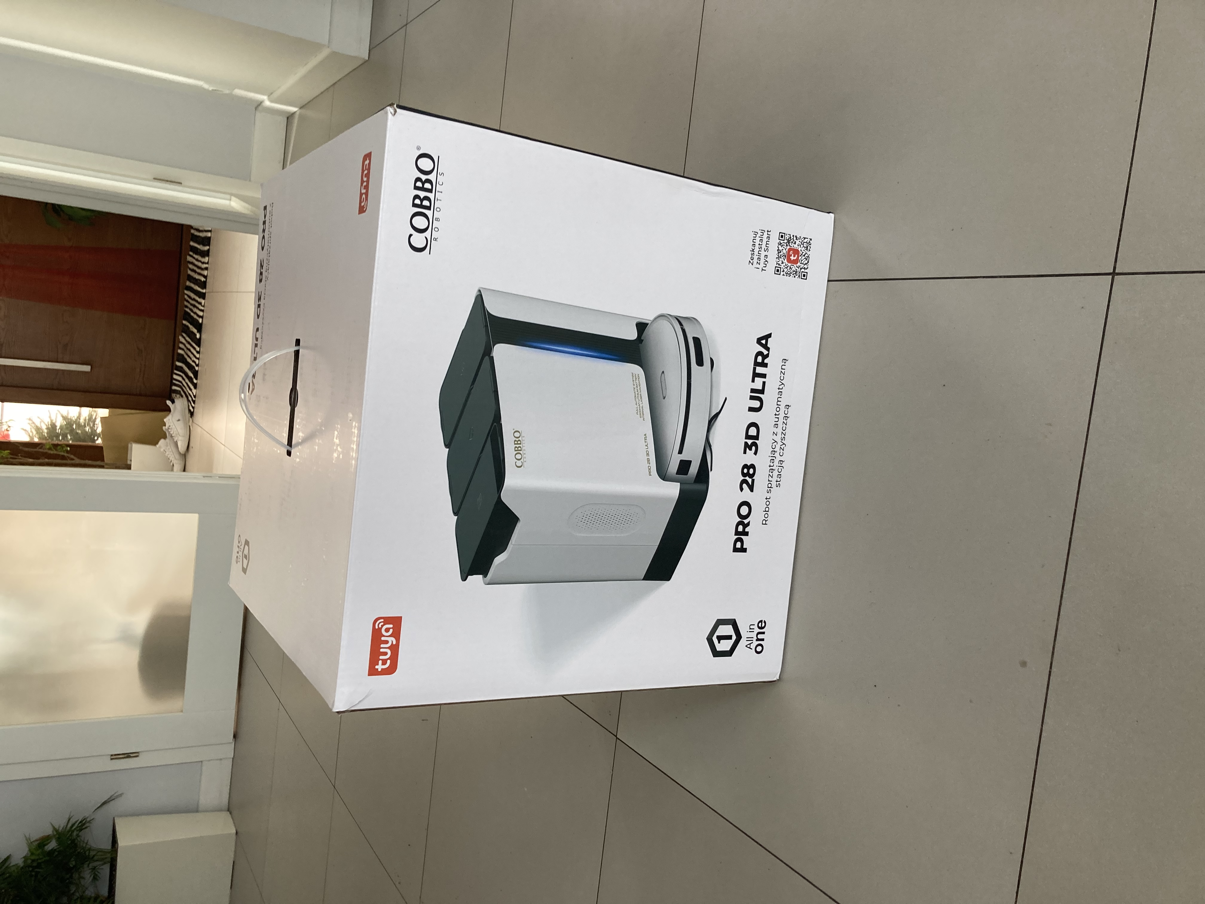 Białe pudełko produktu robota sprzątającego Cobbo Pro 28 3D Ultra stoi na podłodze z płytek.