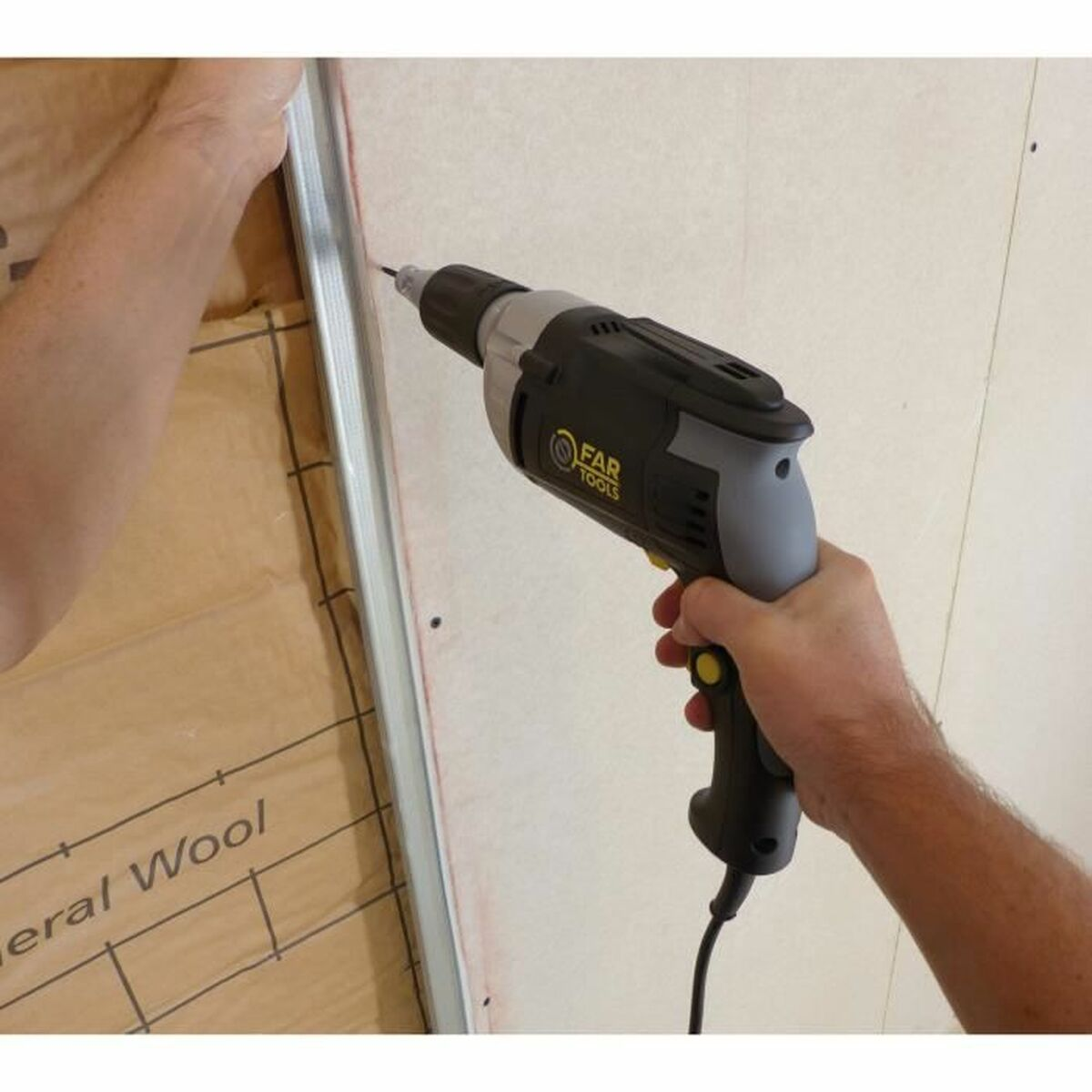 Eine Person bohrt mit einem grauen Elektrowerkzeug in einen Metallrahmen an einer Wand mit Mineralwolle.