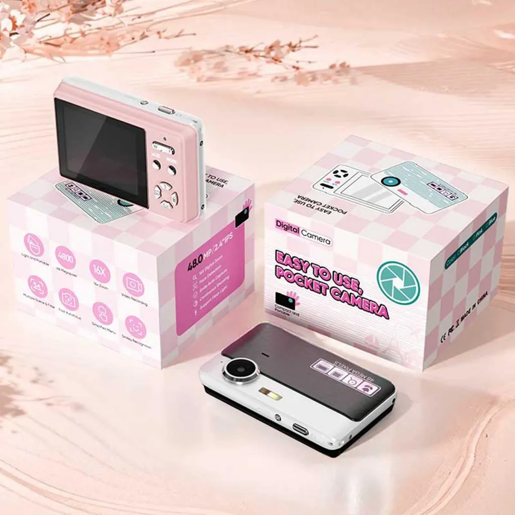 Eine rosa-weiße Digitalkamera mit Bildschirm liegt neben ihrer passenden Geschenkverpackung auf einem Holztisch.