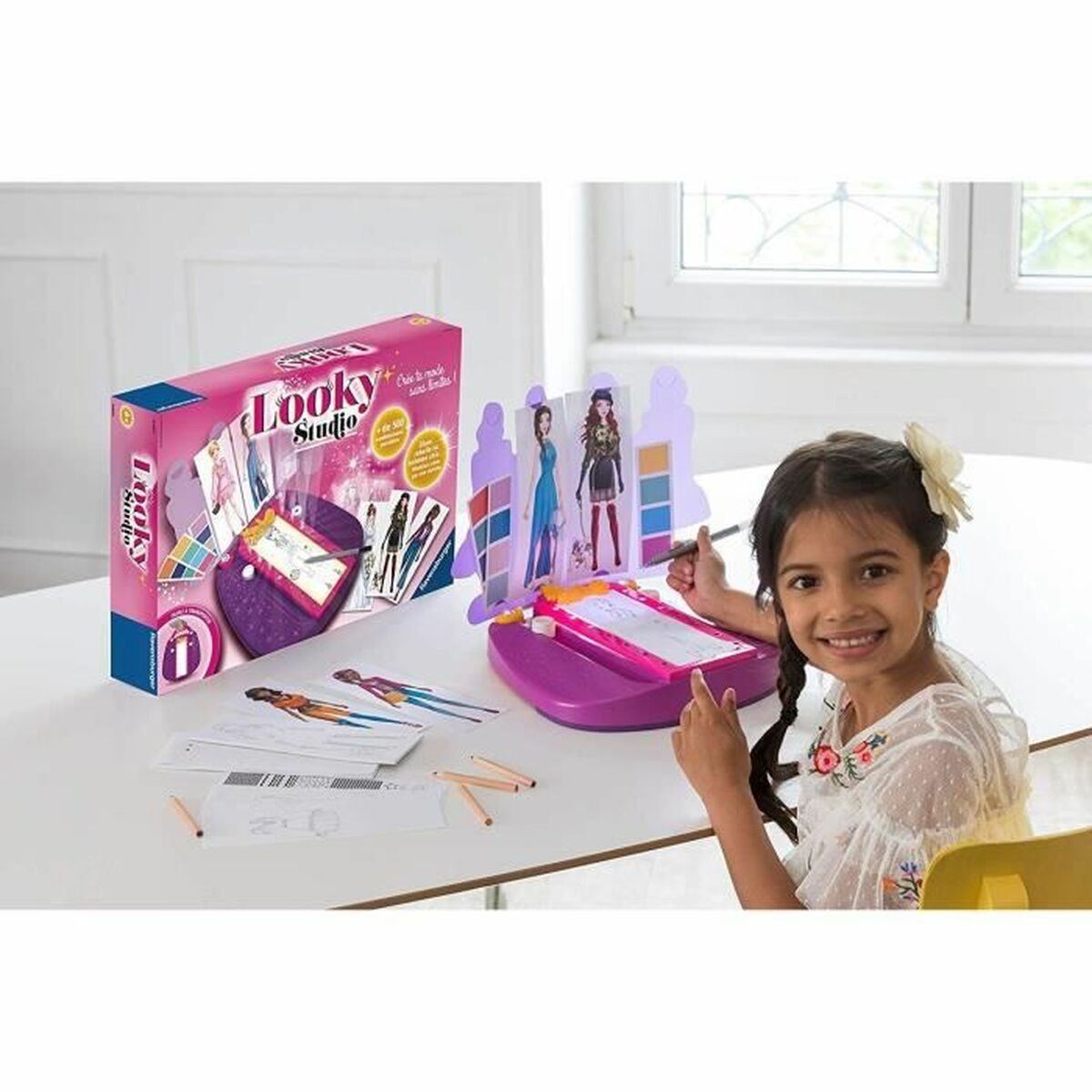 Ein junges Mädchen lächelt und malt mit einem Looky Studio Zeichentisch, während die pinke Spielzeugverpackung daneben steht.