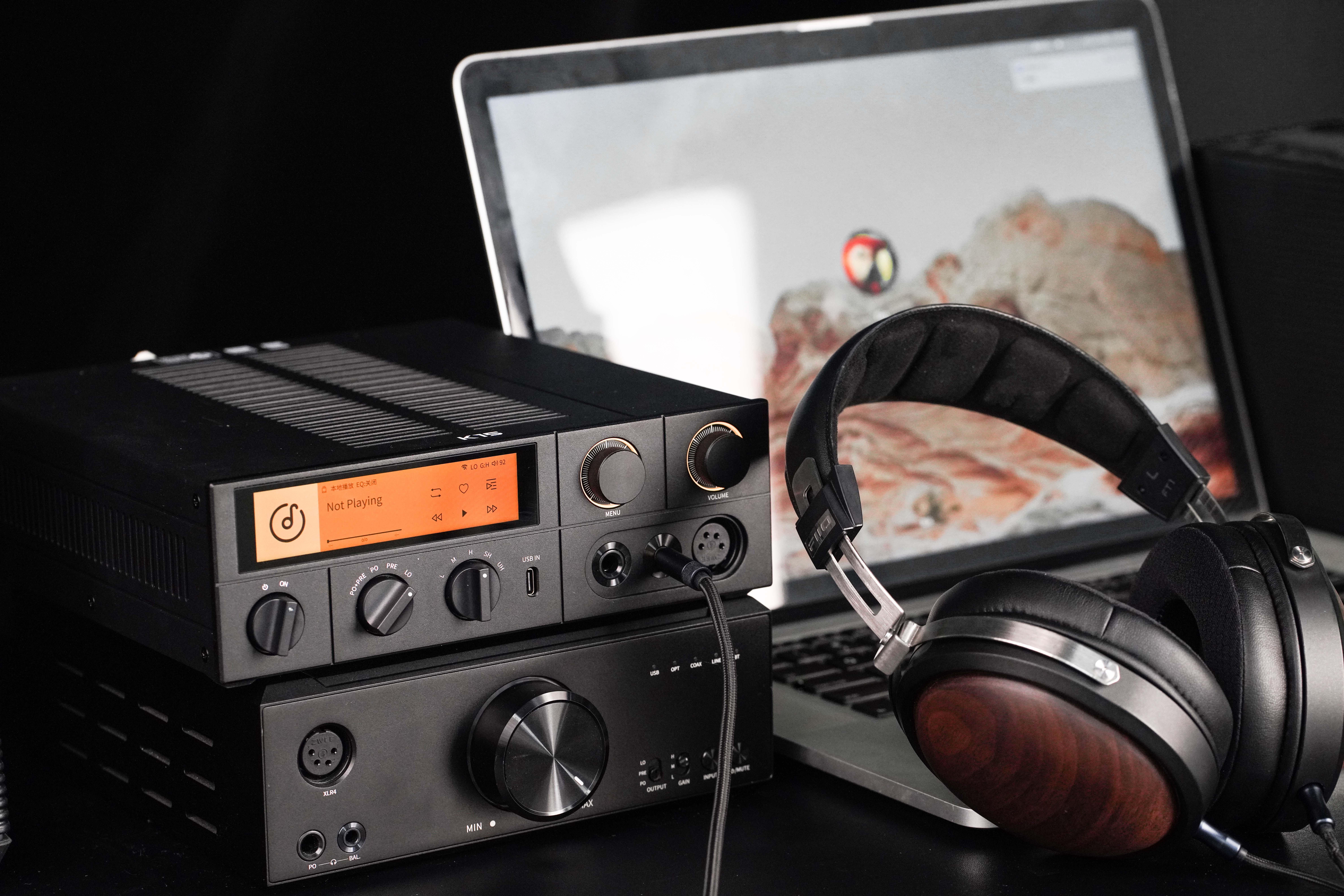 Auriculares negros con detalles de madera frente a un amplificador de audio y un portátil.