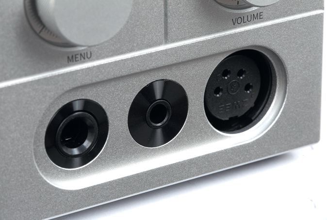 Zbliżenie srebrnego urządzenia audio z trzema czarnymi gniazdami przyłączeniowymi i opisanymi pokrętłami.
