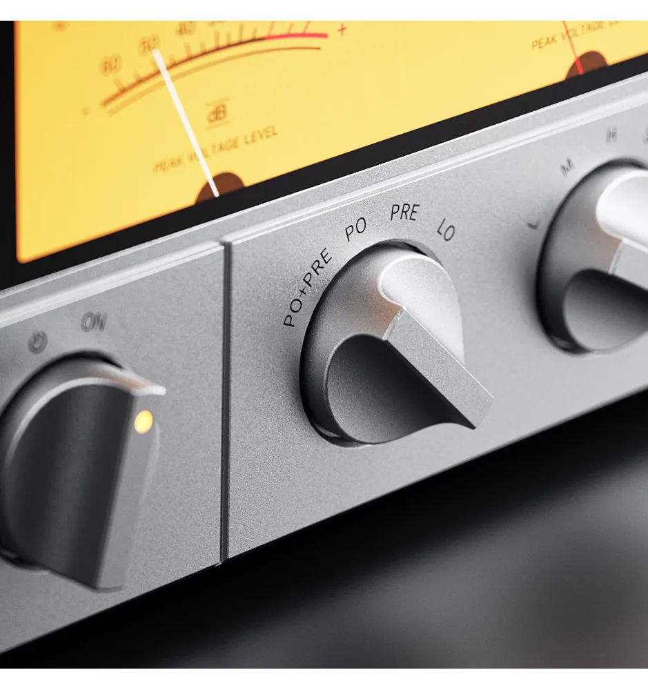 Primer plano de un dispositivo de audio plateado con perillas de control y un medidor VU iluminado en amarillo.