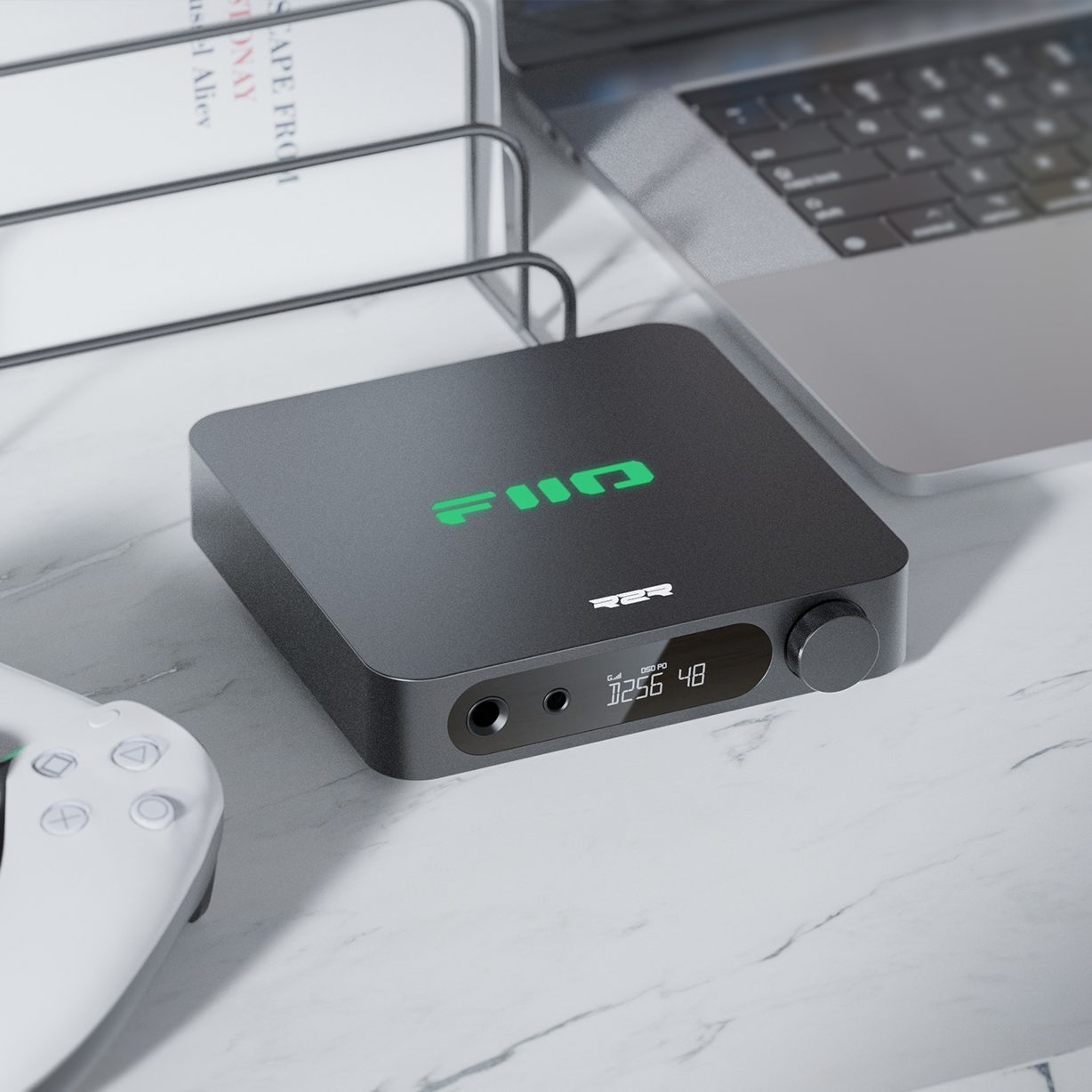 Czarne urządzenie audio FiiO na marmurowym biurku obok laptopa, kontrolera i stojaka na dokumenty.
