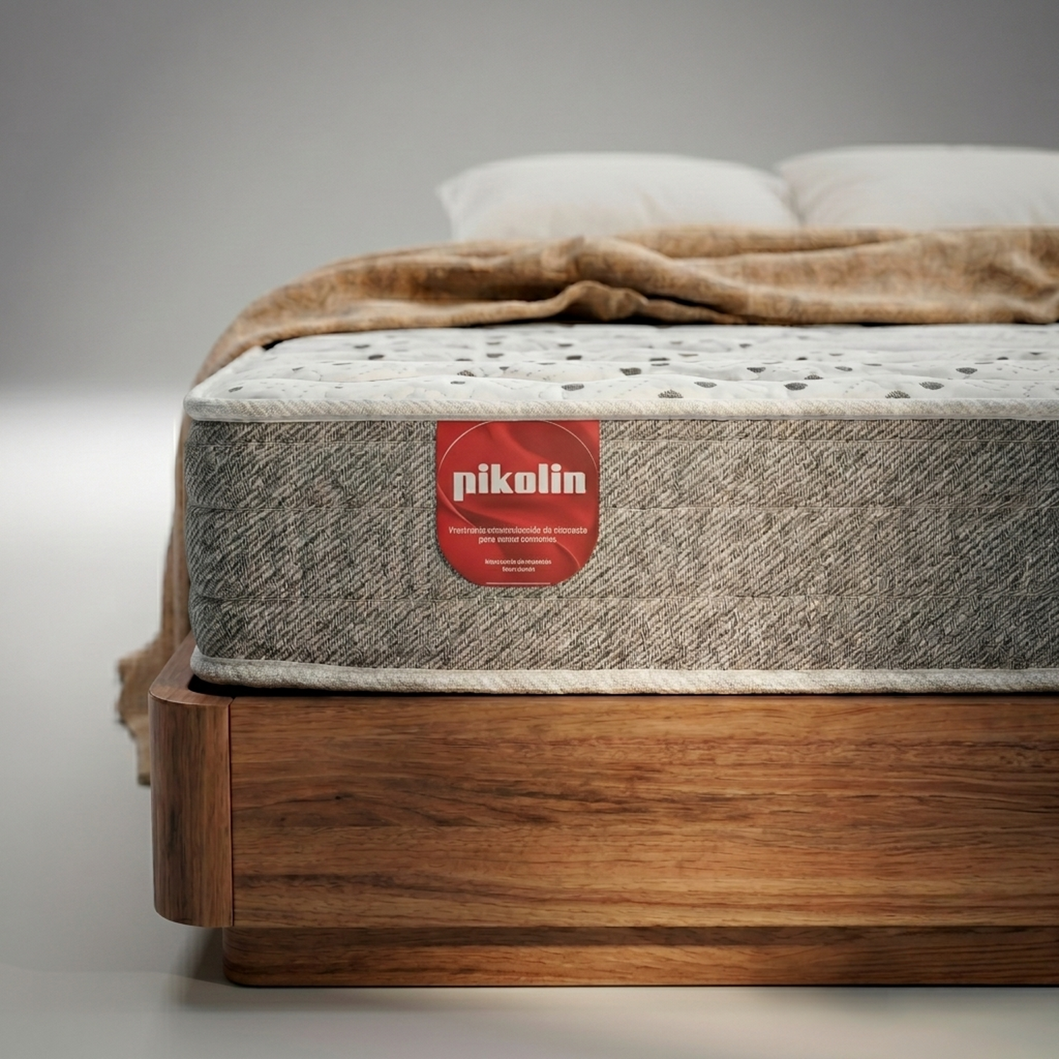 Un colchón Pikolin sobre una base de madera con etiqueta roja, cubierto con manta y almohadas.