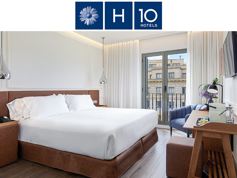 Habitación de hotel moderna con una cama grande, ropa de cama blanca, suelo de madera y vistas a la ciudad.