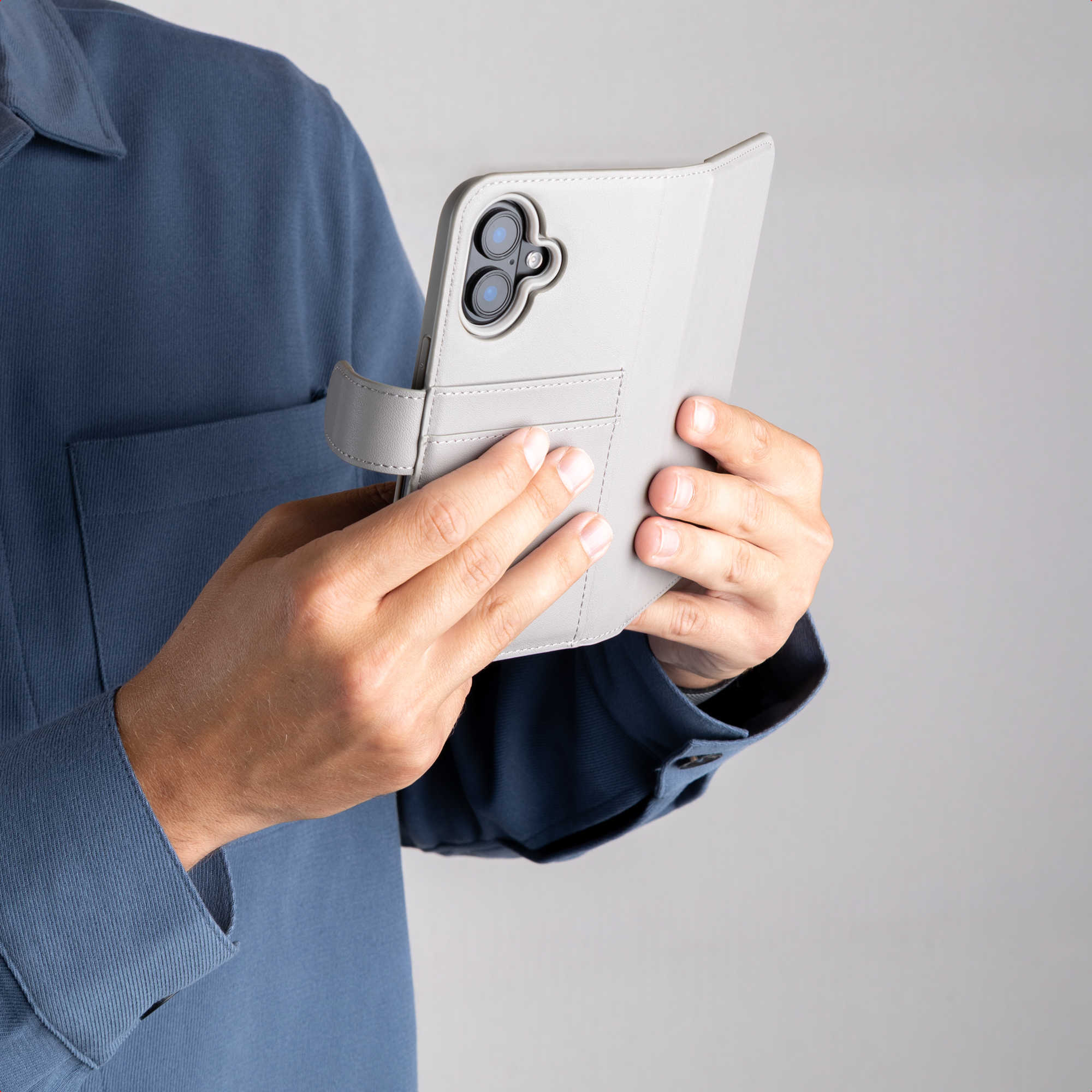 Eine Person im blauen Hemd hält ein Smartphone mit grauer Klapphülle und dualer Kamera.