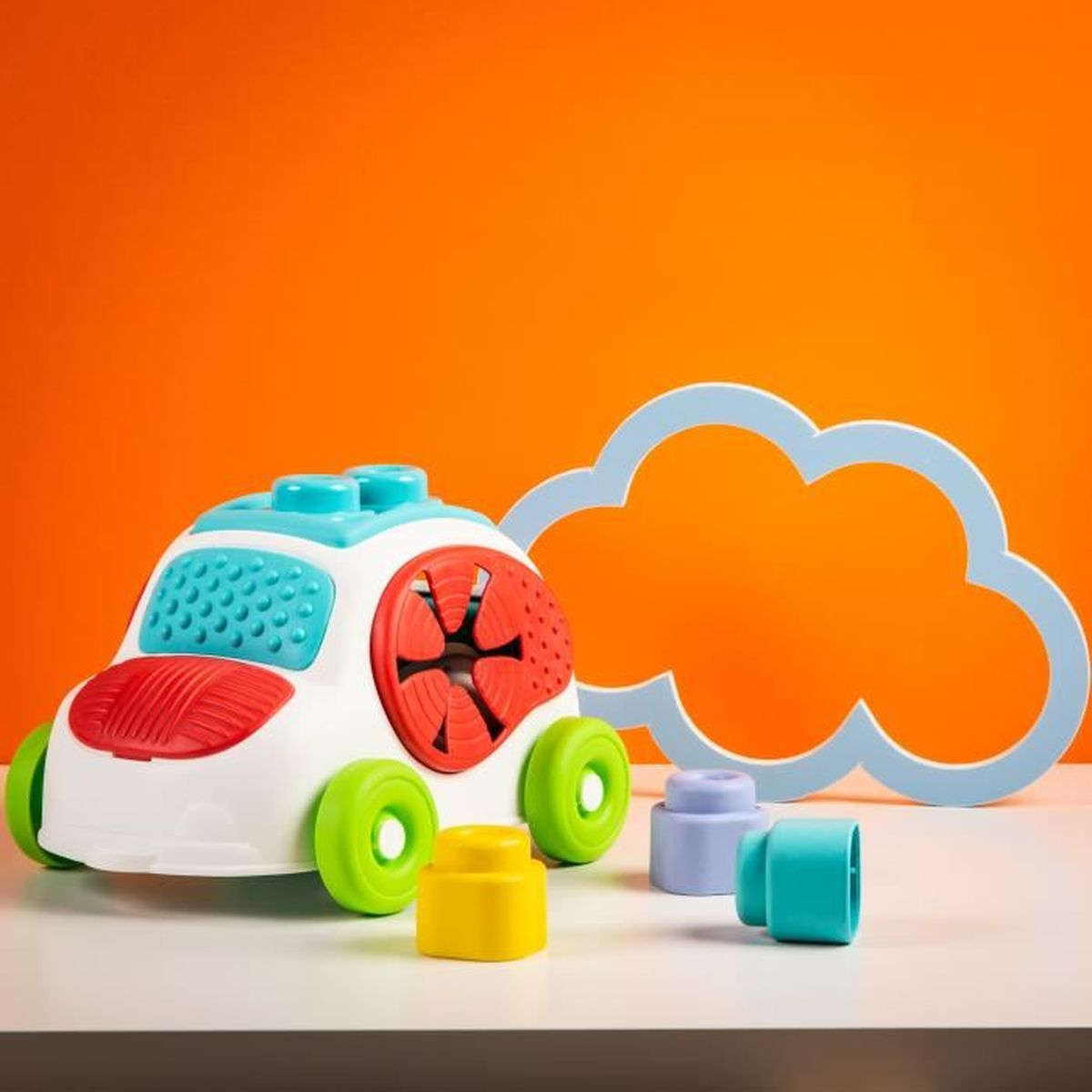 Ein weißes Spielzeugauto mit bunten Rädern und Teilen steht vor einem orangen Hintergrund mit einer hellblauen Wolke.