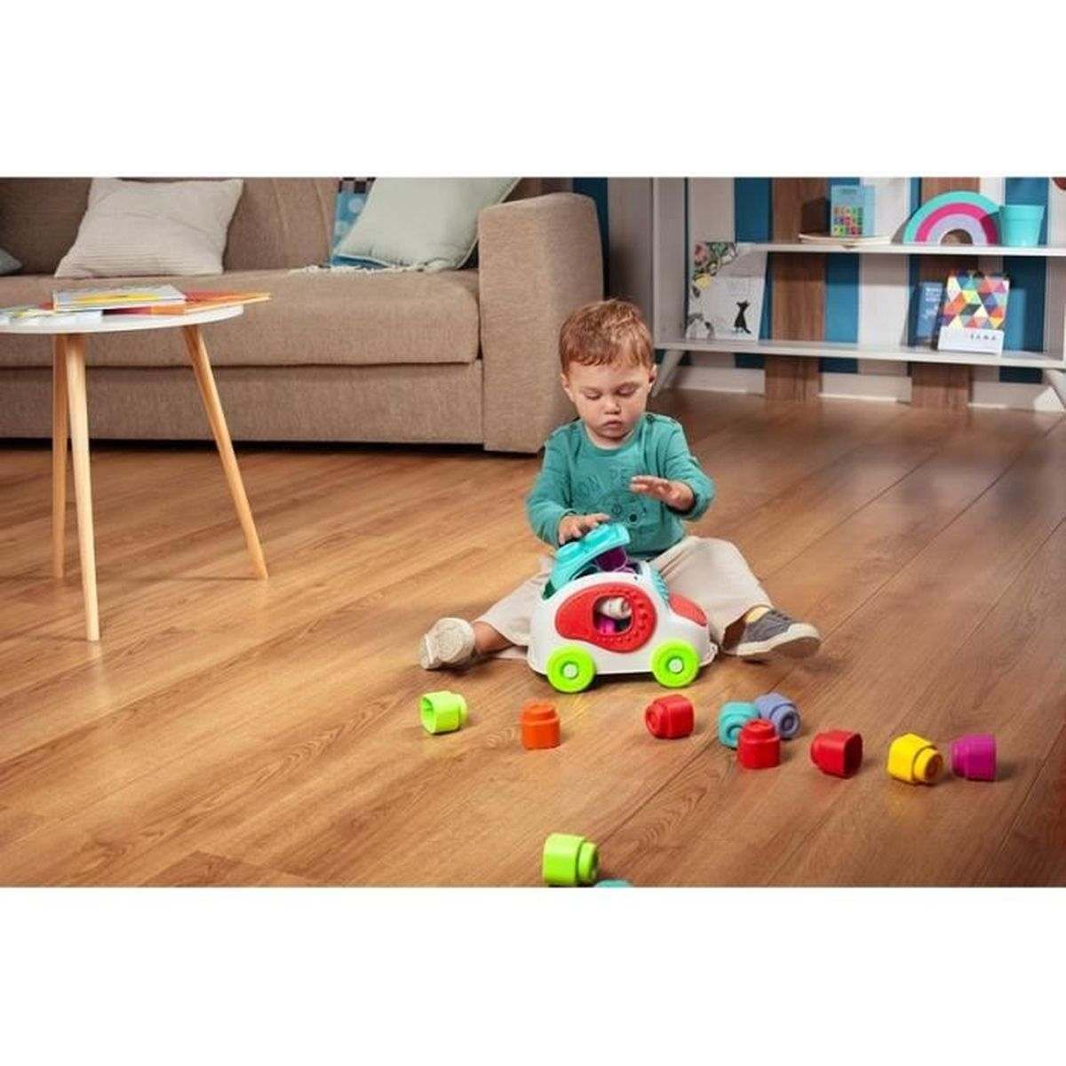 Ein Kleinkind spielt mit einem Spielzeugauto und bunten Klötzen auf einem Holzboden.