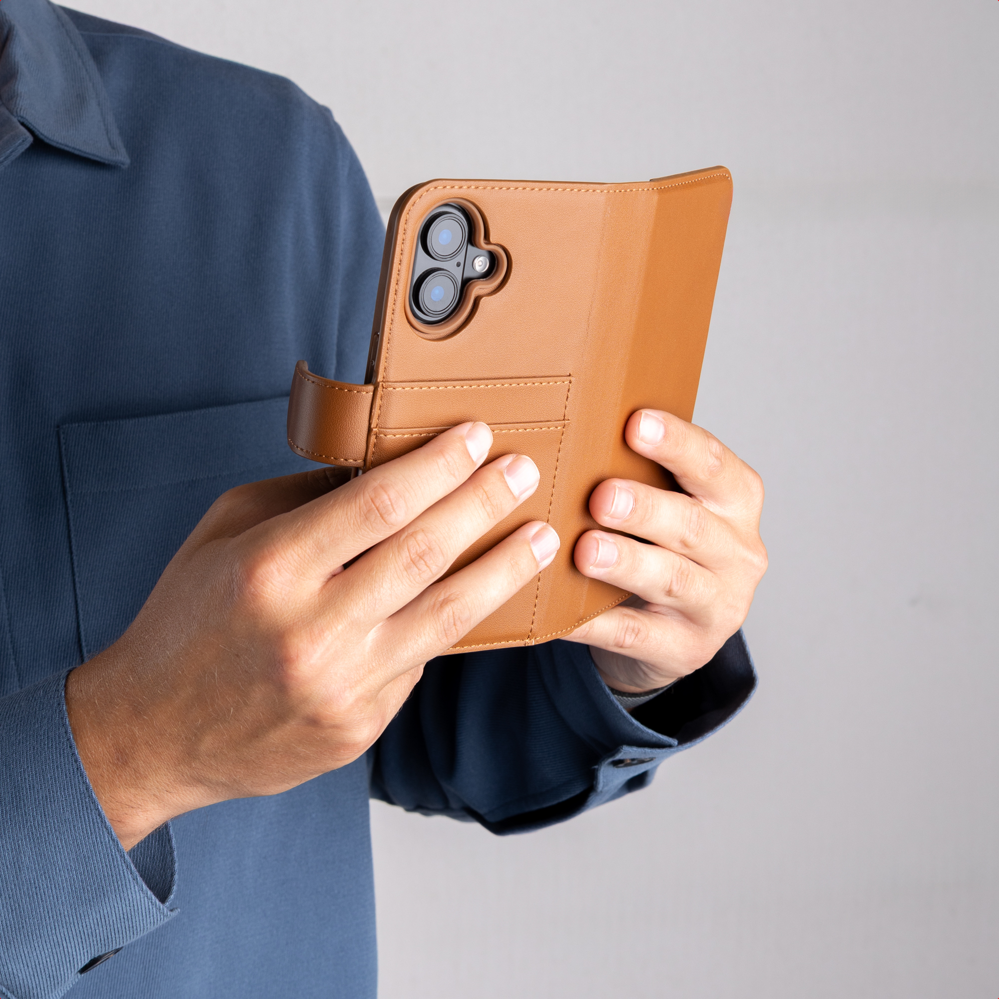 Una persona con camisa azul sostiene un smartphone con funda de cuero marrón, mostrando la parte trasera.