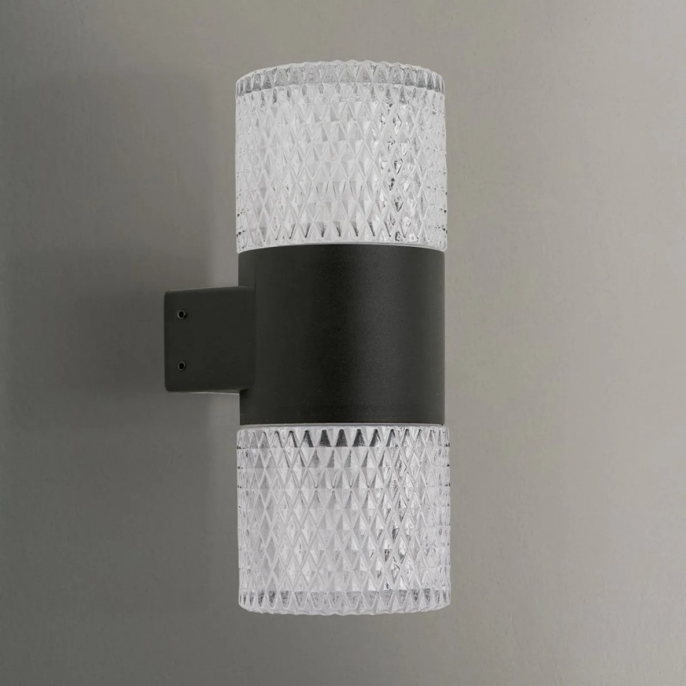 Moderne zylindrische Wandleuchte mit schwarzem Mittelteil und geriffeltem Glas oben und unten auf grauem Grund.