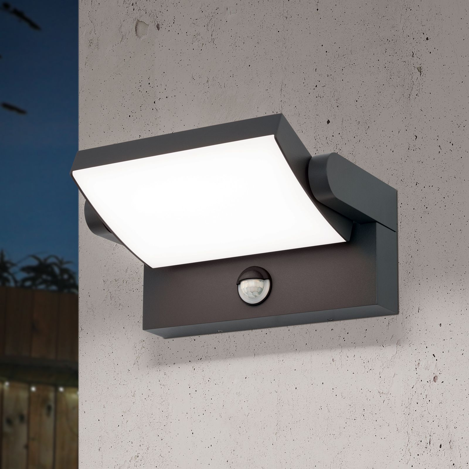 Moderne schwarze Wandlampe mit weißer Leuchtfläche und integriertem Bewegungsmelder an einer Betonwand.
