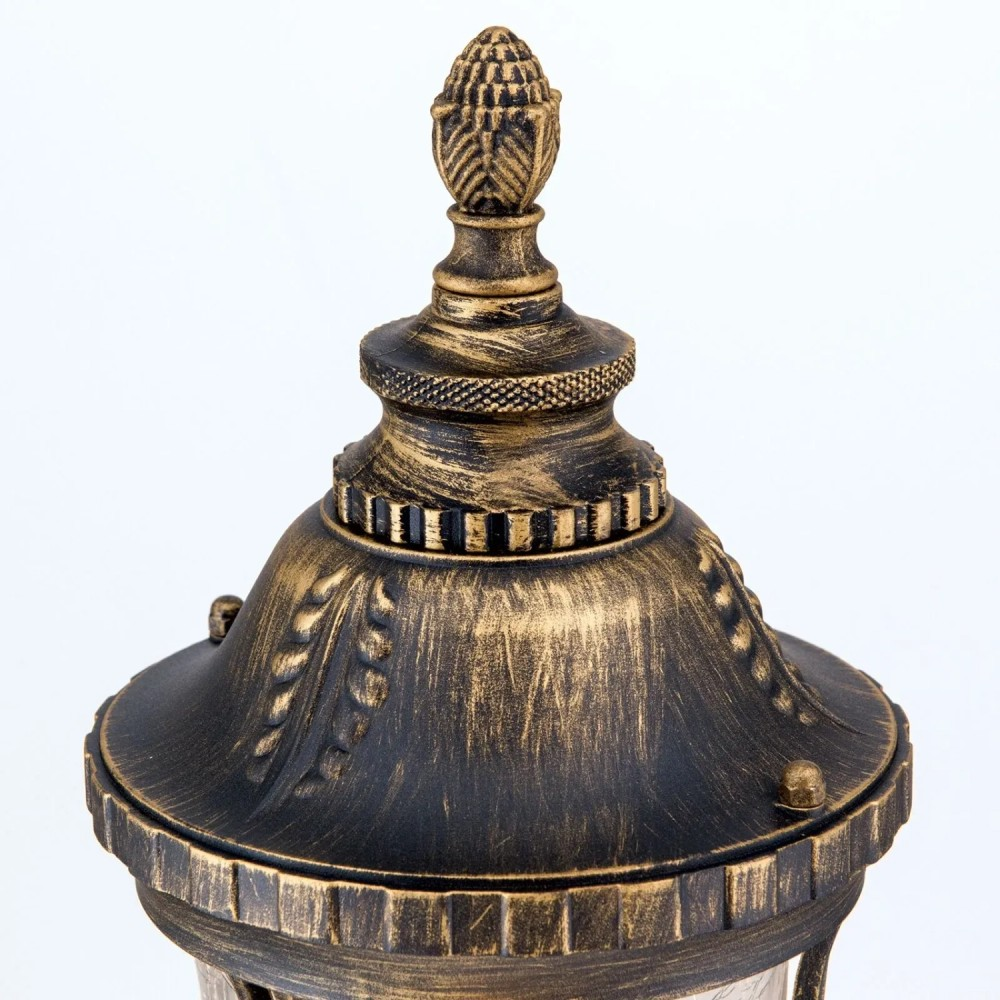 Verzierte antike goldene und schwarze Lampenkappe mit einem Tannenzapfen-Aufsatz auf weißem Hintergrund.