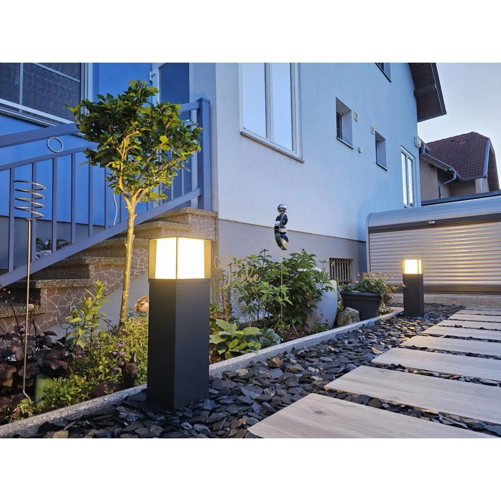 Ein leuchtender Gartenweg mit Steinplatten und beleuchteten Pollerleuchten neben einem hellblauen Haus.