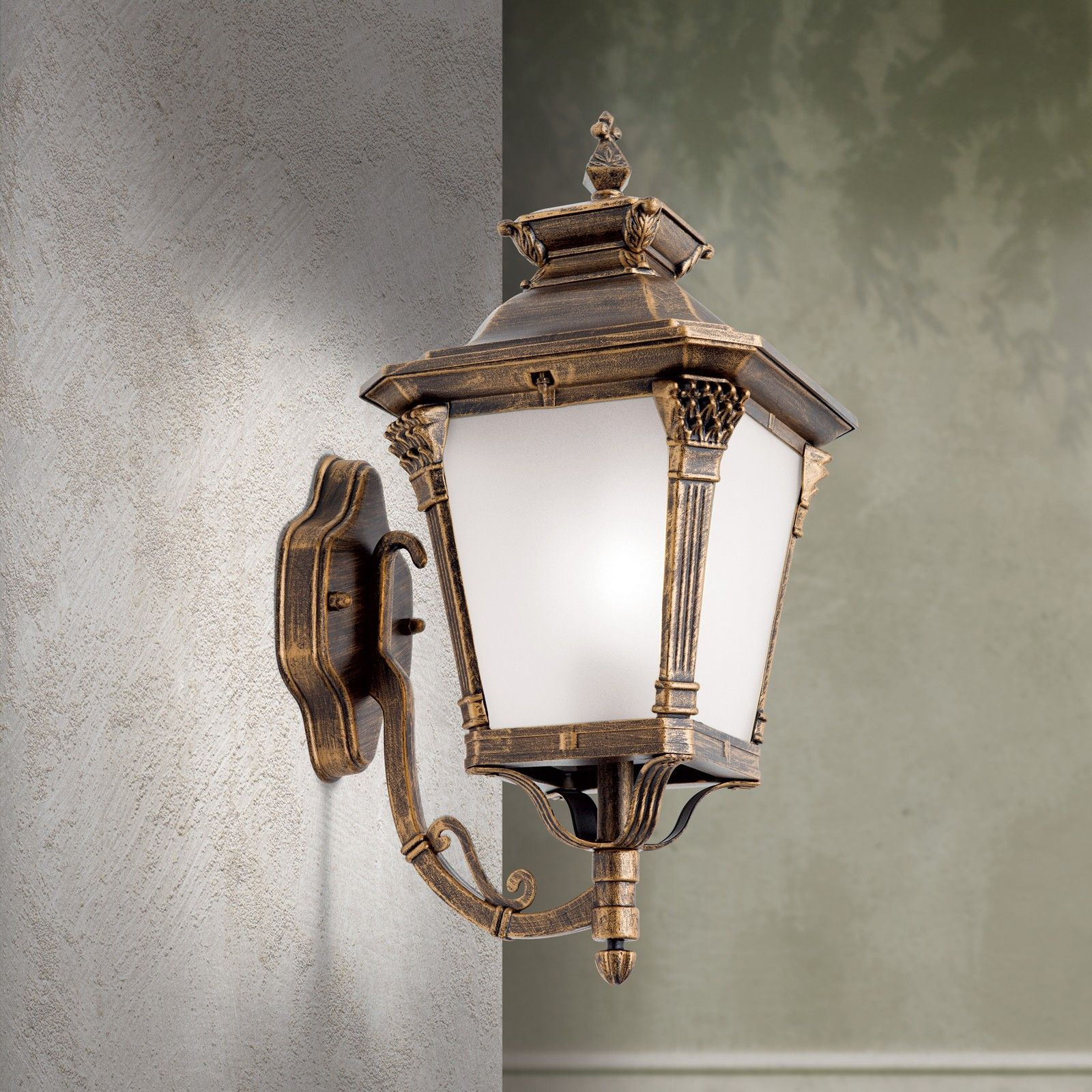 Eine antike, gold-braune Wandlaterne mit weißem Glas hängt an einer strukturierten Wand.