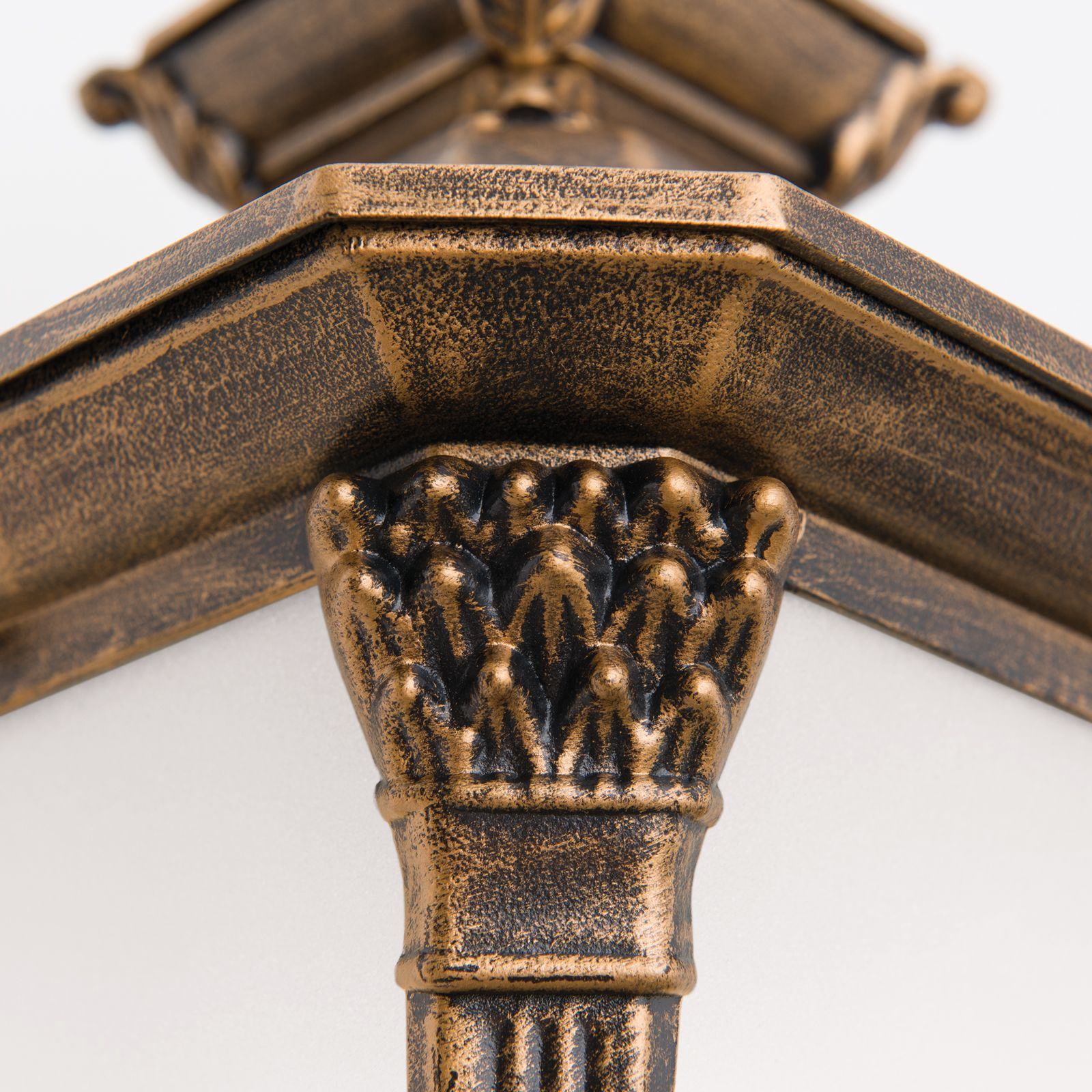 Nahaufnahme einer bronzefarbenen Lampe mit verzierten, klassischen Mustern auf weißem Hintergrund.