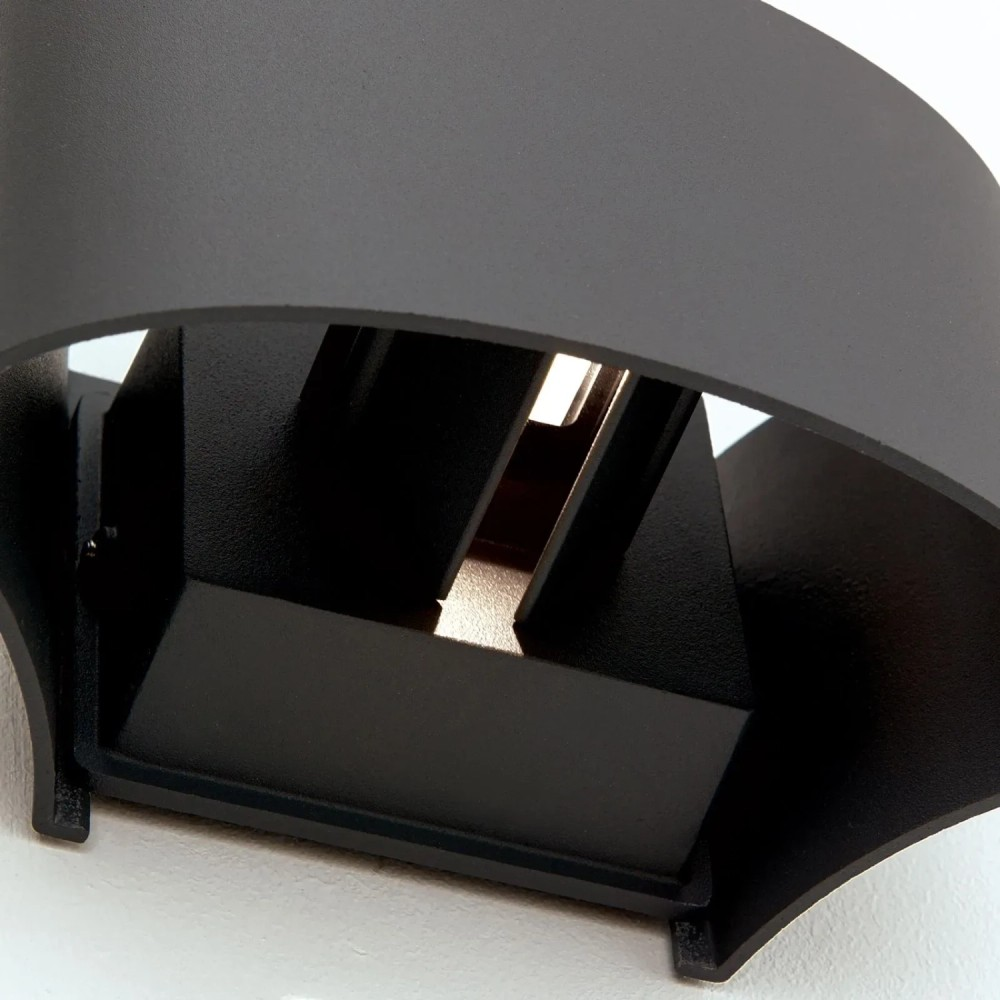 Eine moderne schwarze Wandlampe mit gebogenem Metallgehäuse und Innenbeleuchtung an einer weißen Wand.