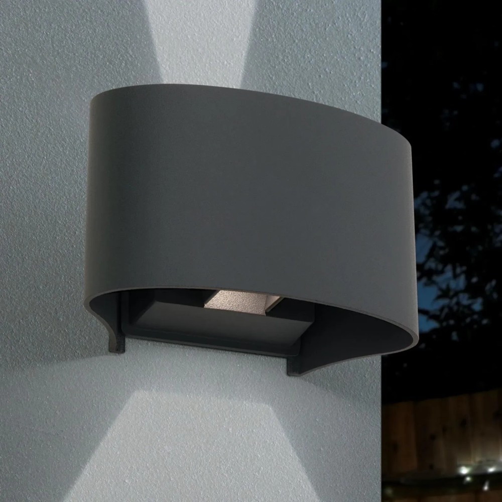 Eine schwarze, gebogene Wandlampe leuchtet nach oben und unten an eine helle Wand.