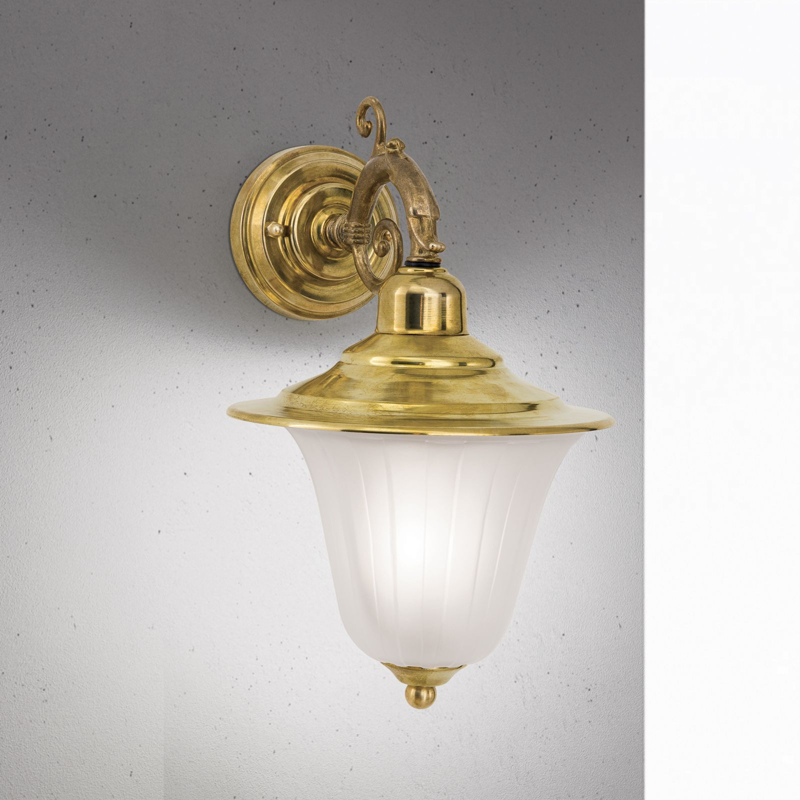 Eine Messing-Wandleuchte mit mattiertem Glasschirm an einer grauen Betonwand.