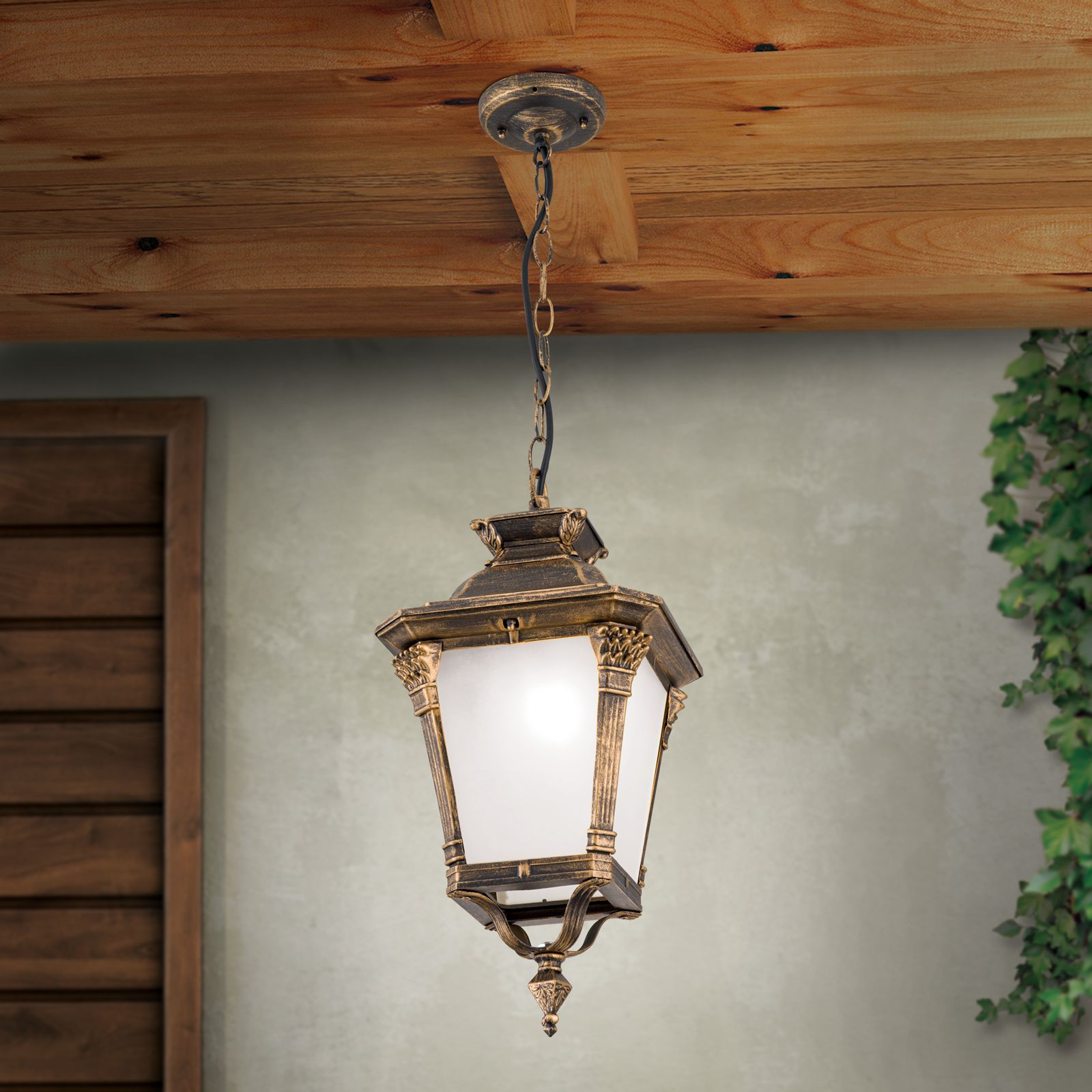 Eine antike, hängende Deckenleuchte mit mattem Glas und gold-schwarzem Rahmen unter einer Holzdecke.