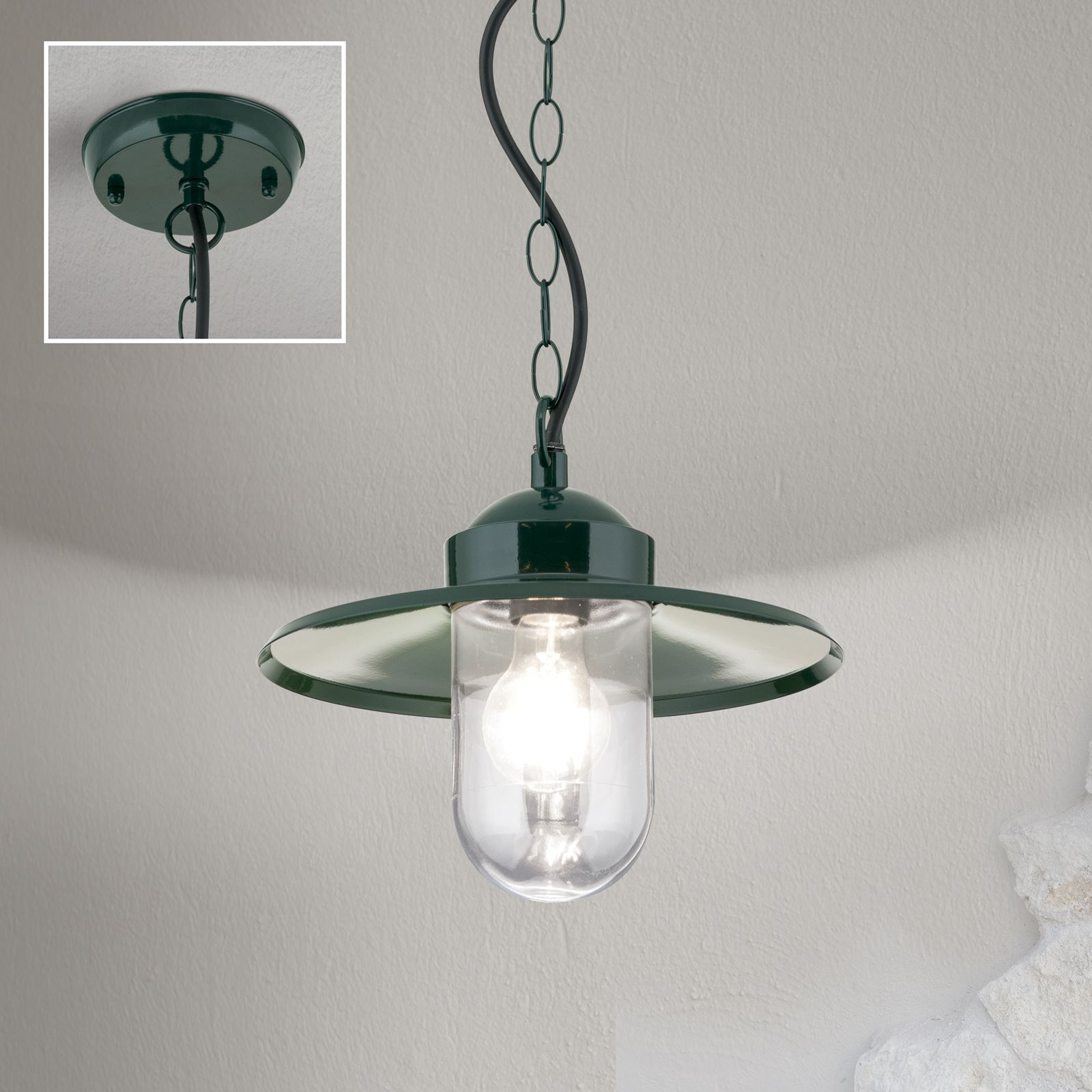 Eine dunkelgrüne Pendelleuchte mit klarem Glasschirm hängt an einer Kette vor hellgrauer Wand, mit Deckenhalterung im Ausschnitt.