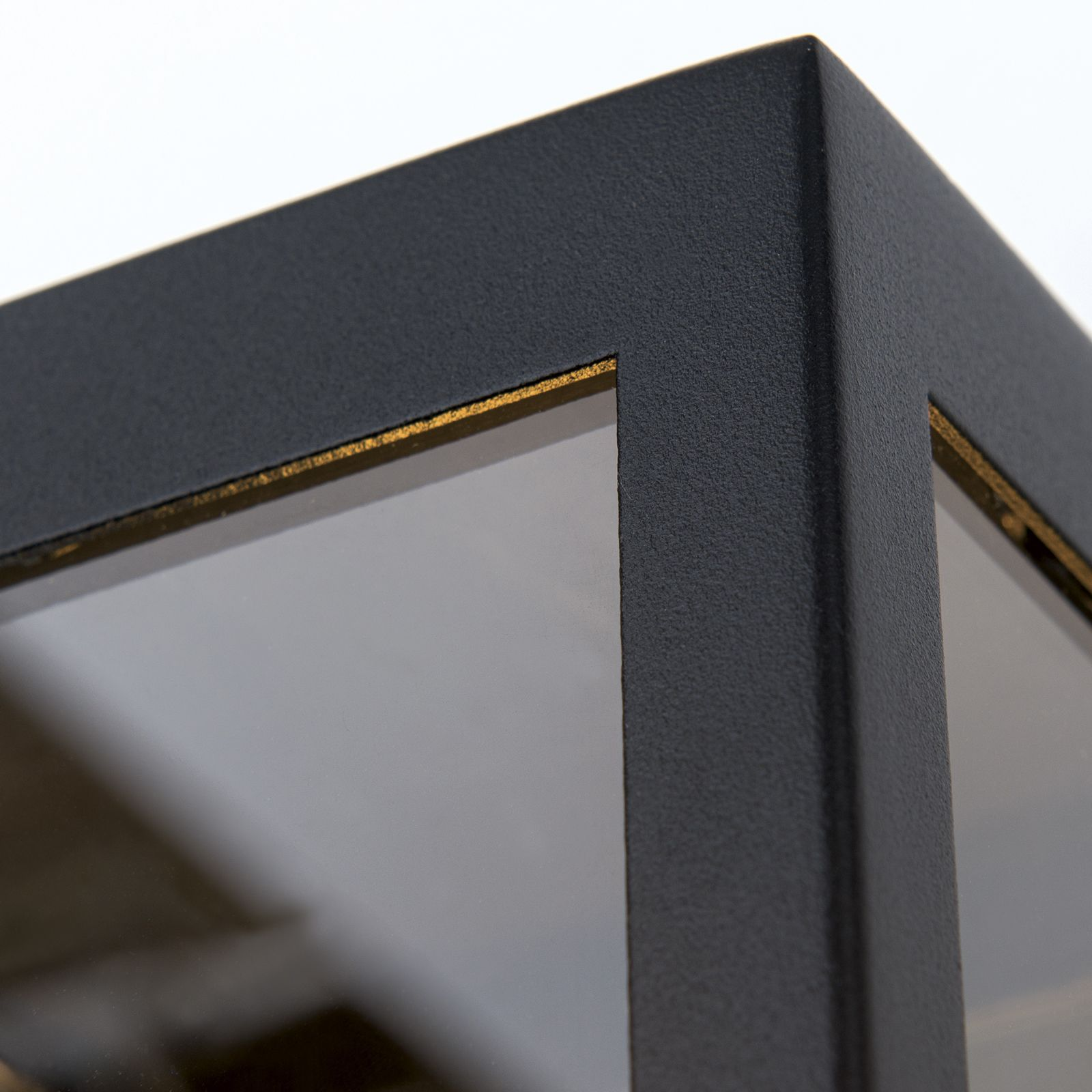 Nahaufnahme einer schwarzen, strukturierten Metallrahmen-Ecke mit goldenem Innenrand.