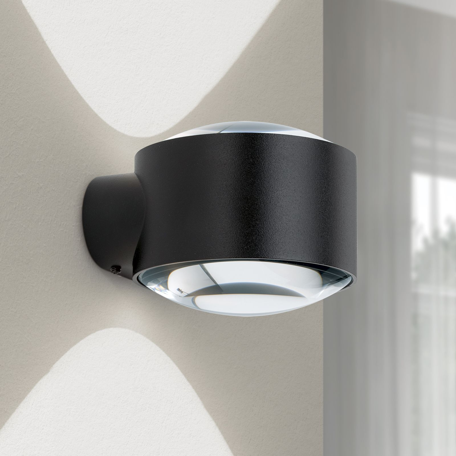 Moderne schwarze Wandleuchte mit klaren Glaslinsen wirft helles Licht auf die Wand.