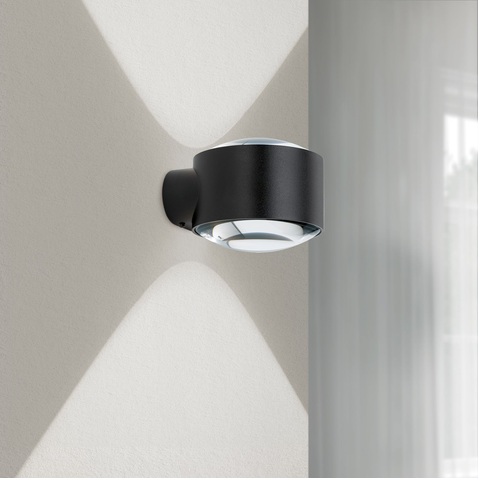 Eine schwarze Wandlampe strahlt Licht nach oben und unten an eine helle Wand.