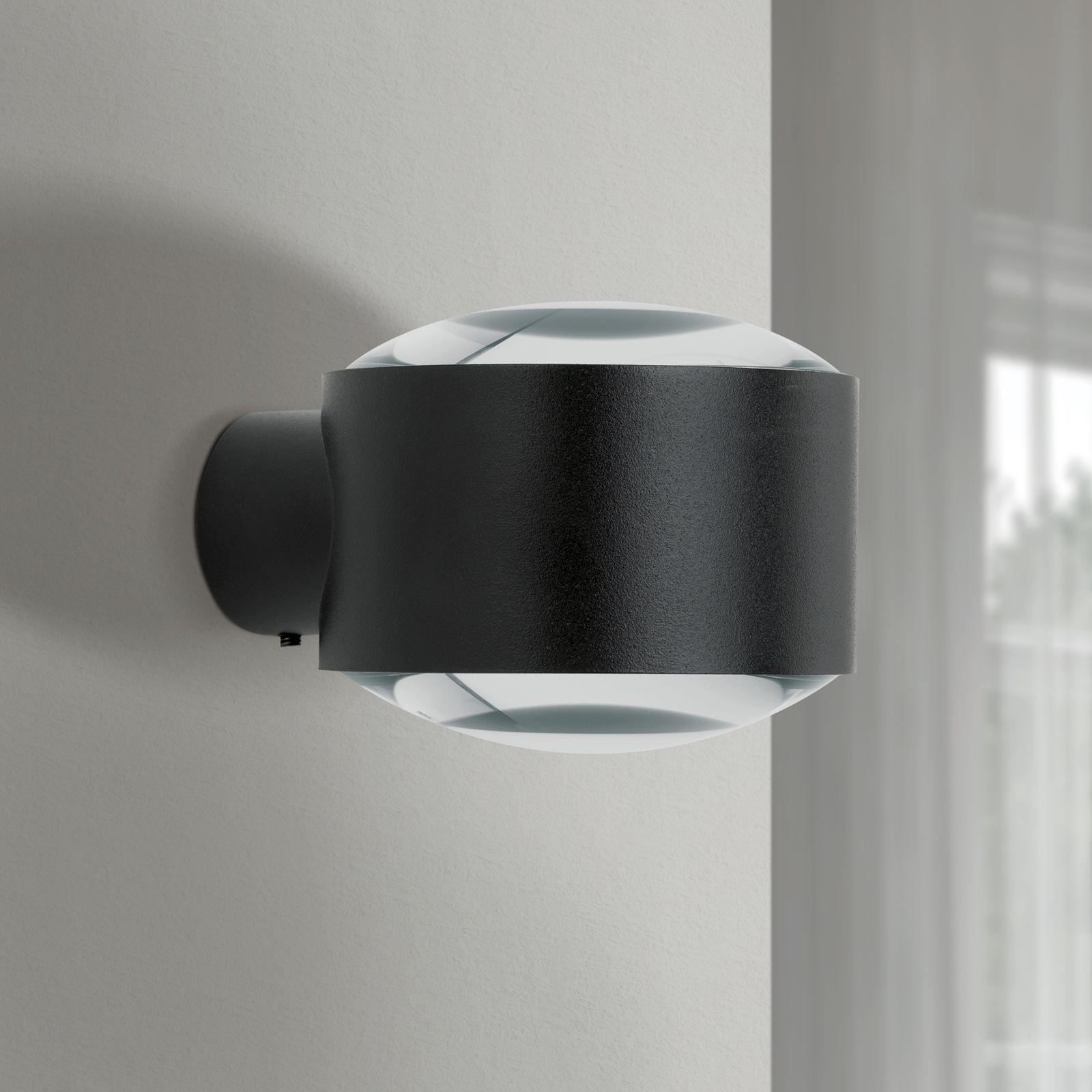 Moderne schwarze Wandleuchte mit klaren Glaselementen an einer hellen Wand.