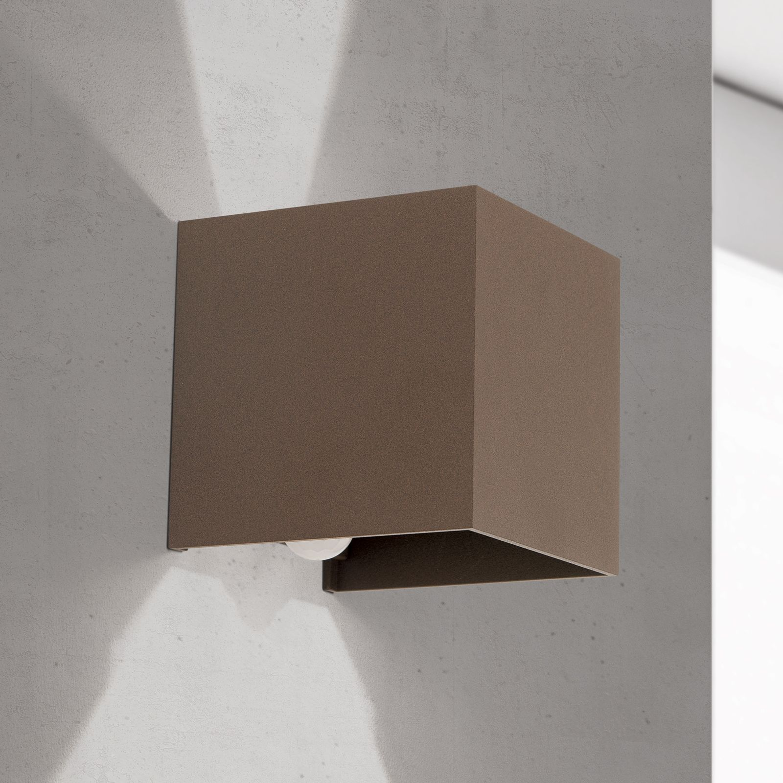 Eine braune, quaderförmige Wandleuchte ist an einer grauen Wand montiert und wirft Licht nach oben und unten.