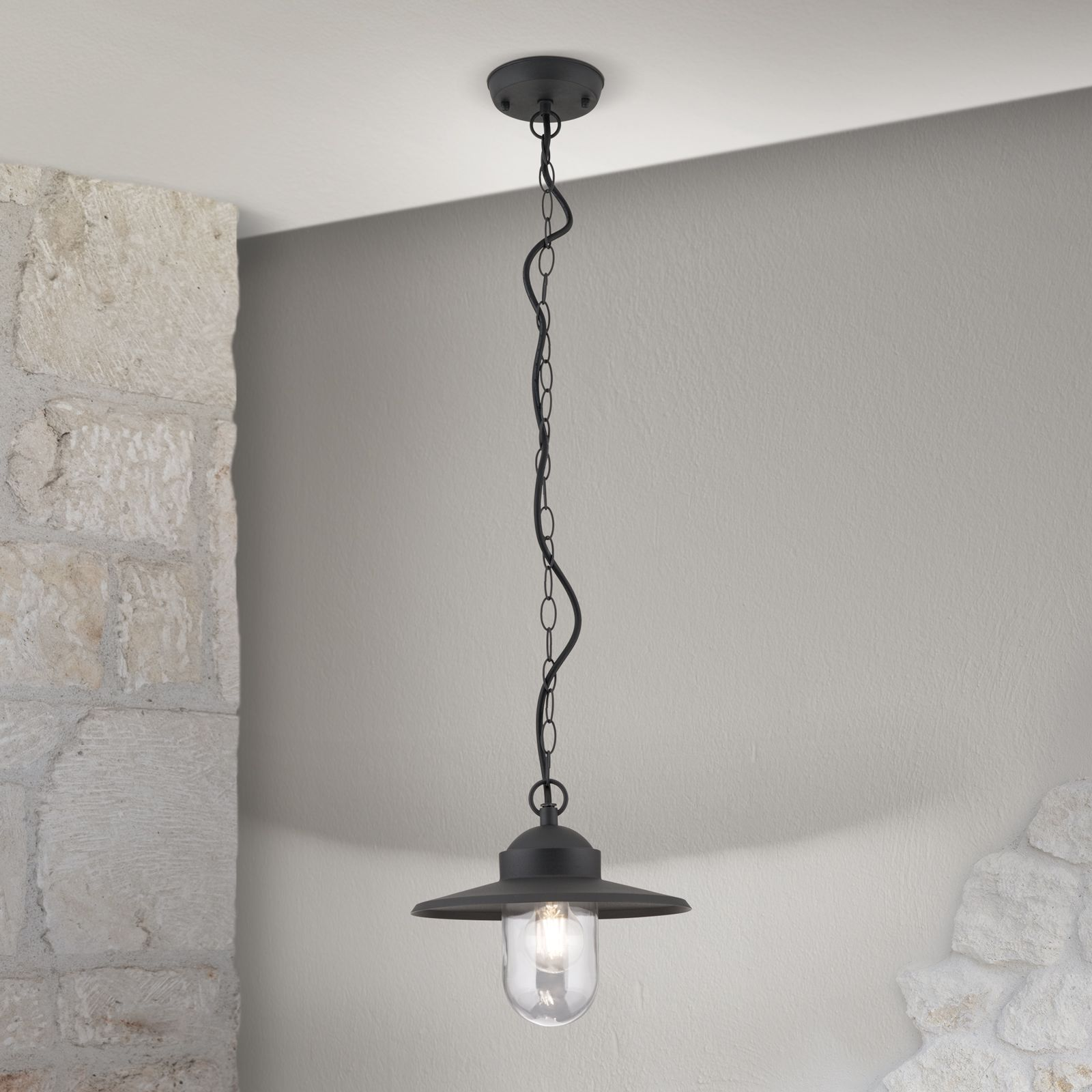 Eine schwarze Pendelleuchte hängt vor einer Steinwand an der Decke.